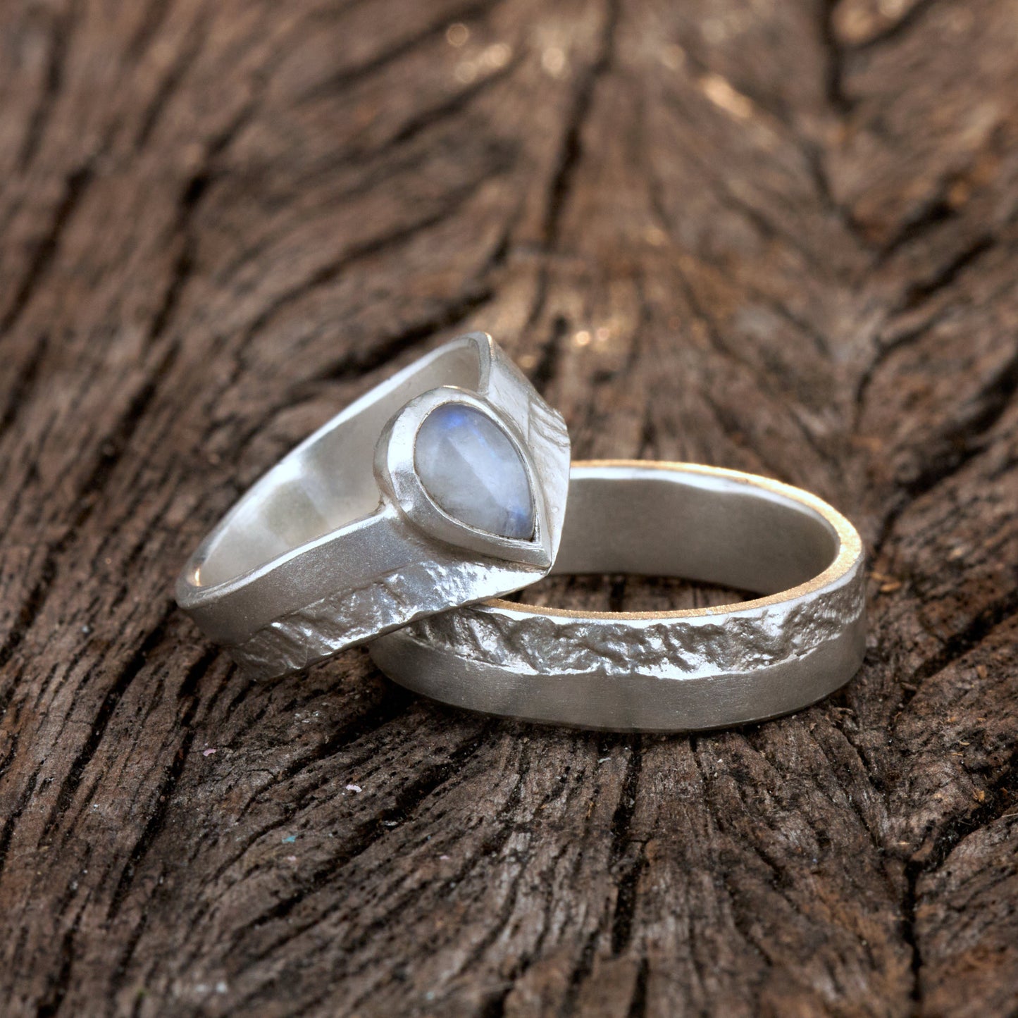 Hochwertiges Eheringe Set aus massivem 925 Sterling Silber mit kontrastreicher Oberfläche halb matt und halb retikuliert. Der Damenring in eleganter Wishbone V-Form trägt einen handgefassten Regenbogen-Mondstein im Tropfenschliff 9x6 mm mit blauem Schimmer. Der Herrenring ist 6x2 mm breit und spiegelt das maritime nordische Design wider. Handgefertigte Markenware aus der Goldschmiede Silberschweif für Paare die exklusiven Edelsteinschmuck und archaische Strukturen suchen