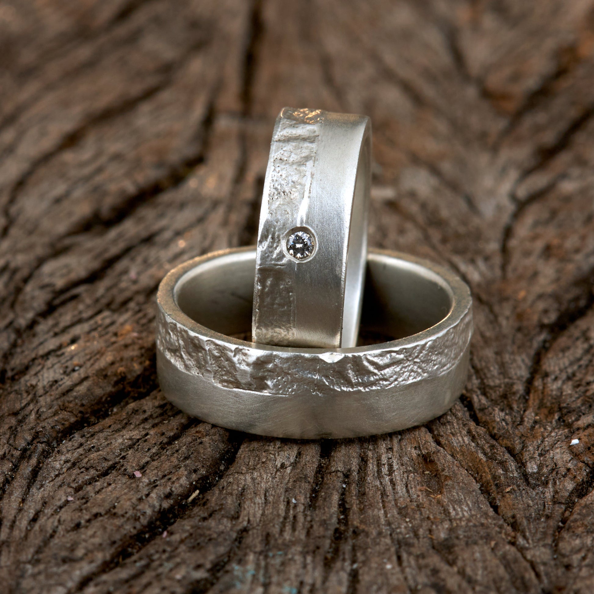 Massive Trauringe aus 925 Silber handgefertigt. Eheringe mit markanter Schieferstruktur retikuliert im Kontrast zu mattierten Oberflächen. Damenring ca. 6mm breit mit einem bündig gefassten 2mm Brillanten (TW/si). Herrenring ca. 6mm breit, massiv und charakterstark. Einzigartiges Partnerring-Set mit organischer Textur, inspiriert von natürlichem Fels. Handgemacht in eigener Werkstatt in Deutschland, keine CNC-Massenware. Hochwertige Unikate für Individualisten