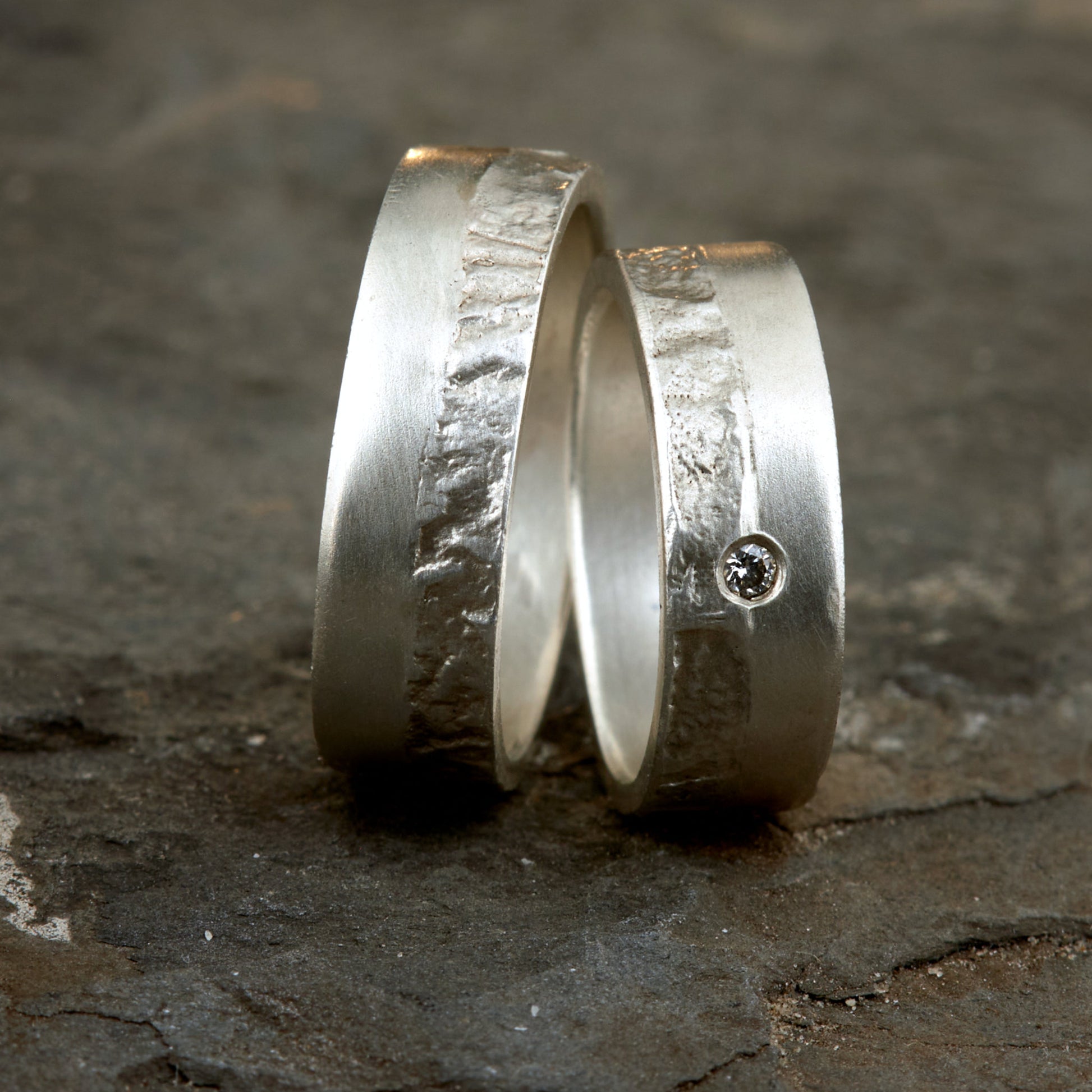 Massive Trauringe aus 925 Silber handgefertigt. Eheringe mit markanter Schieferstruktur retikuliert im Kontrast zu mattierten Oberflächen. Damenring ca. 6mm breit mit einem bündig gefassten 2mm Brillanten (TW/si). Herrenring ca. 6mm breit, massiv und charakterstark. Einzigartiges Partnerring-Set mit organischer Textur, inspiriert von natürlichem Fels. Handgemacht in eigener Werkstatt in Deutschland, keine CNC-Massenware. Hochwertige Unikate für Individualisten