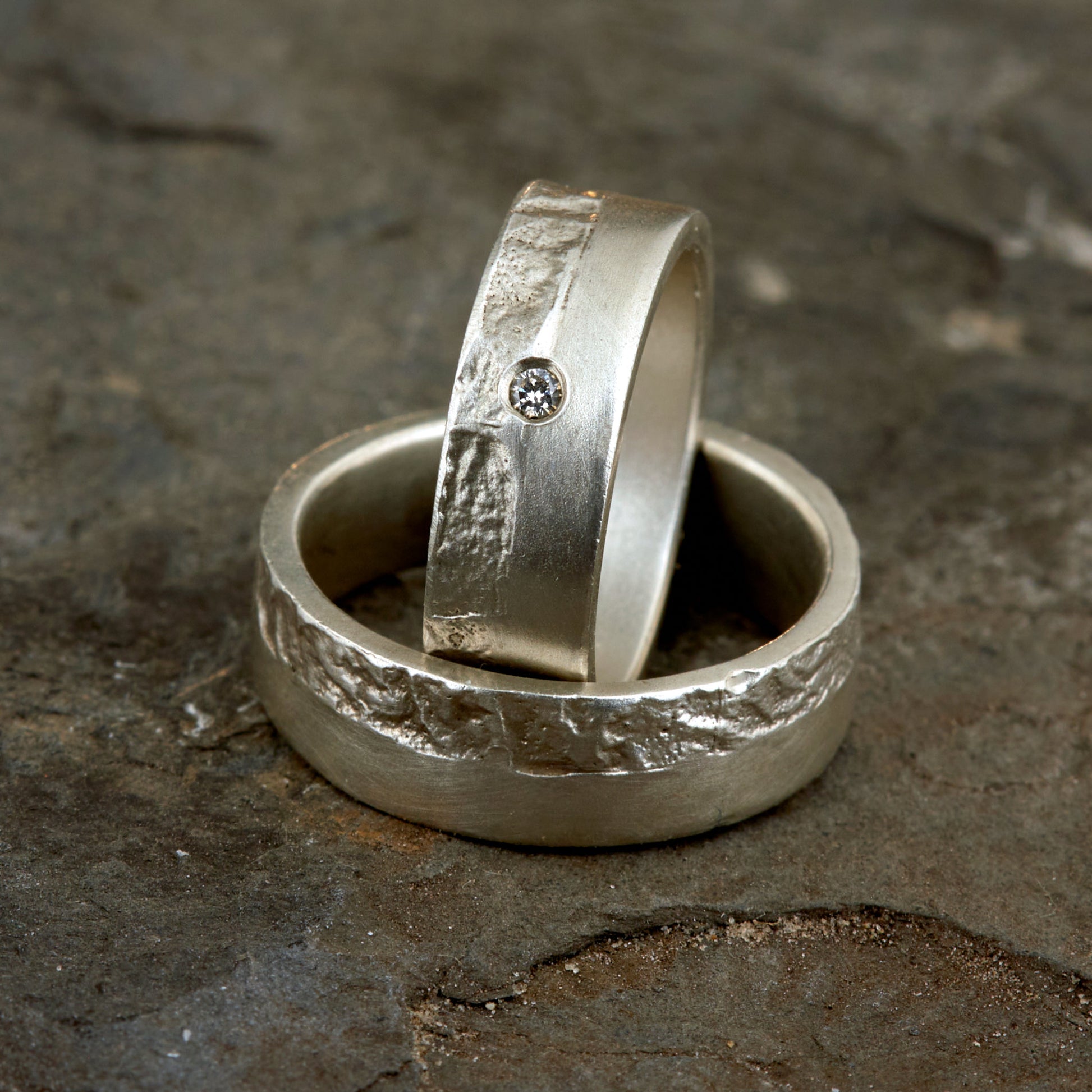 Massive Trauringe aus 925 Silber handgefertigt. Eheringe mit markanter Schieferstruktur retikuliert im Kontrast zu mattierten Oberflächen. Damenring ca. 6mm breit mit einem bündig gefassten 2mm Brillanten (TW/si). Herrenring ca. 6mm breit, massiv und charakterstark. Einzigartiges Partnerring-Set mit organischer Textur, inspiriert von natürlichem Fels. Handgemacht in eigener Werkstatt in Deutschland, keine CNC-Massenware. Hochwertige Unikate für Individualisten