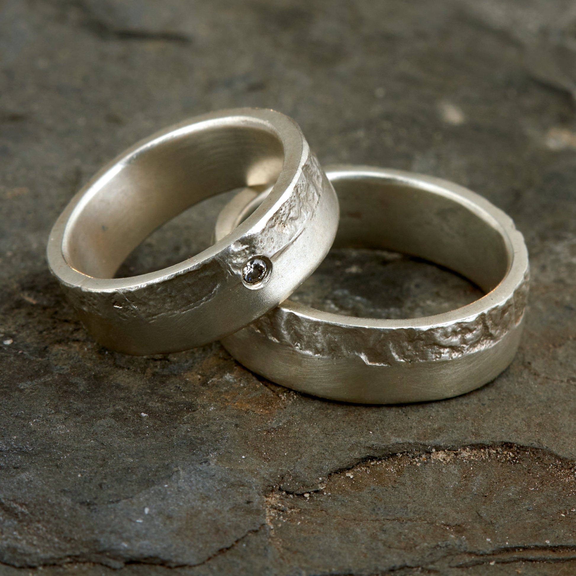 Massive Trauringe aus 925 Silber handgefertigt. Eheringe mit markanter Schieferstruktur retikuliert im Kontrast zu mattierten Oberflächen. Damenring ca. 6mm breit mit einem bündig gefassten 2mm Brillanten (TW/si). Herrenring ca. 6mm breit, massiv und charakterstark. Einzigartiges Partnerring-Set mit organischer Textur, inspiriert von natürlichem Fels. Handgemacht in eigener Werkstatt in Deutschland, keine CNC-Massenware. Hochwertige Unikate für Individualisten