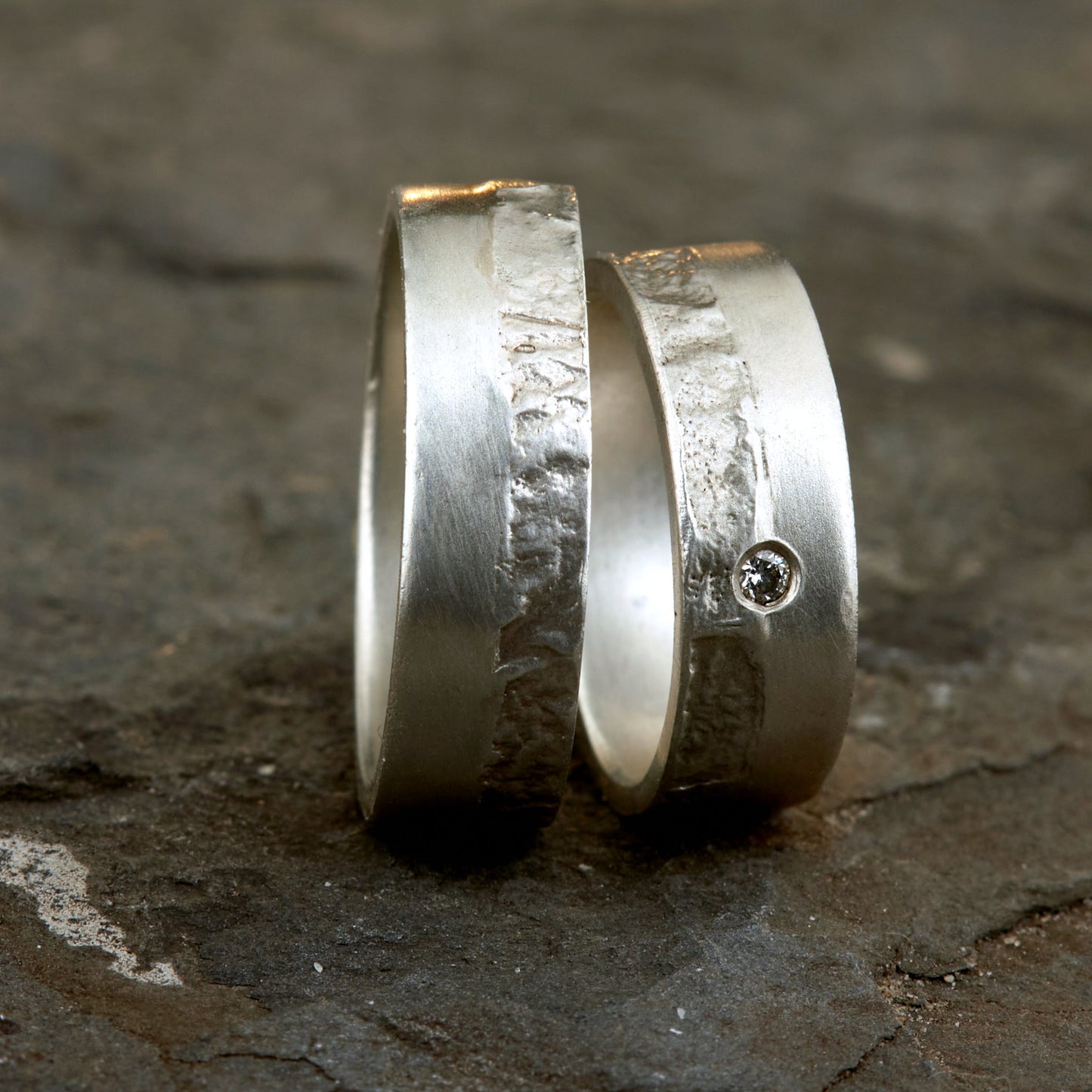 Massive Trauringe aus 925 Silber handgefertigt. Eheringe mit markanter Schieferstruktur retikuliert im Kontrast zu mattierten Oberflächen. Damenring ca. 6mm breit mit einem bündig gefassten 2mm Brillanten (TW/si). Herrenring ca. 6mm breit, massiv und charakterstark. Einzigartiges Partnerring-Set mit organischer Textur, inspiriert von natürlichem Fels. Handgemacht in eigener Werkstatt in Deutschland, keine CNC-Massenware. Hochwertige Unikate für Individualisten