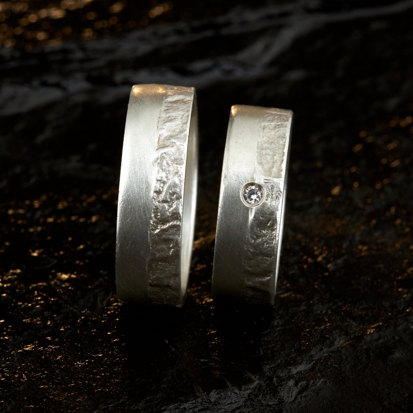 Massive Trauringe aus 925 Silber handgefertigt. Eheringe mit markanter Schieferstruktur retikuliert im Kontrast zu mattierten Oberflächen. Damenring ca. 6mm breit mit einem bündig gefassten 2mm Brillanten (TW/si). Herrenring ca. 6mm breit, massiv und charakterstark. Einzigartiges Partnerring-Set mit organischer Textur, inspiriert von natürlichem Fels. Handgemacht in eigener Werkstatt in Deutschland, keine CNC-Massenware. Hochwertige Unikate für Individualisten