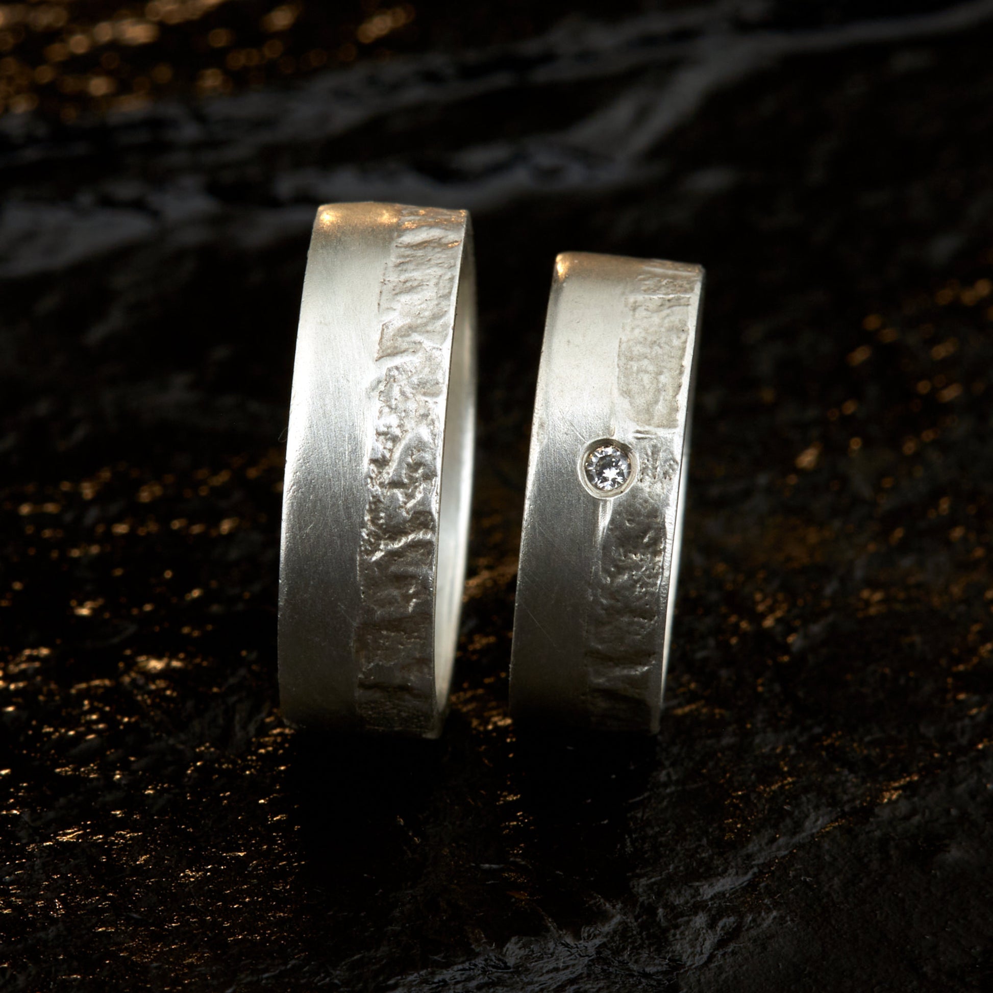 Massive Trauringe aus 925 Silber handgefertigt. Eheringe mit markanter Schieferstruktur retikuliert im Kontrast zu mattierten Oberflächen. Damenring ca. 6mm breit mit einem bündig gefassten 2mm Brillanten (TW/si). Herrenring ca. 6mm breit, massiv und charakterstark. Einzigartiges Partnerring-Set mit organischer Textur, inspiriert von natürlichem Fels. Handgemacht in eigener Werkstatt in Deutschland, keine CNC-Massenware. Hochwertige Unikate für Individualisten