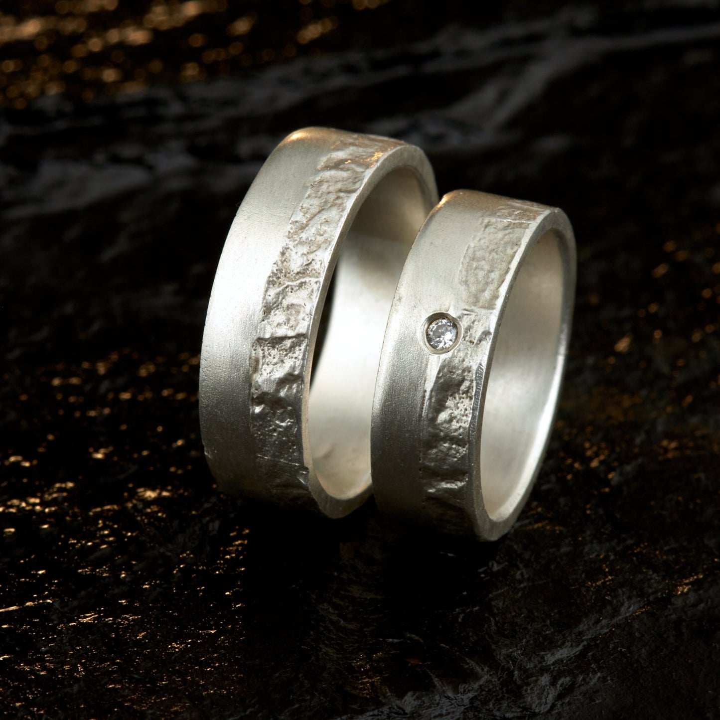 Massive Trauringe aus 925 Silber handgefertigt. Eheringe mit markanter Schieferstruktur retikuliert im Kontrast zu mattierten Oberflächen. Damenring ca. 6mm breit mit einem bündig gefassten 2mm Brillanten (TW/si). Herrenring ca. 6mm breit, massiv und charakterstark. Einzigartiges Partnerring-Set mit organischer Textur, inspiriert von natürlichem Fels. Handgemacht in eigener Werkstatt in Deutschland, keine CNC-Massenware. Hochwertige Unikate für Individualisten