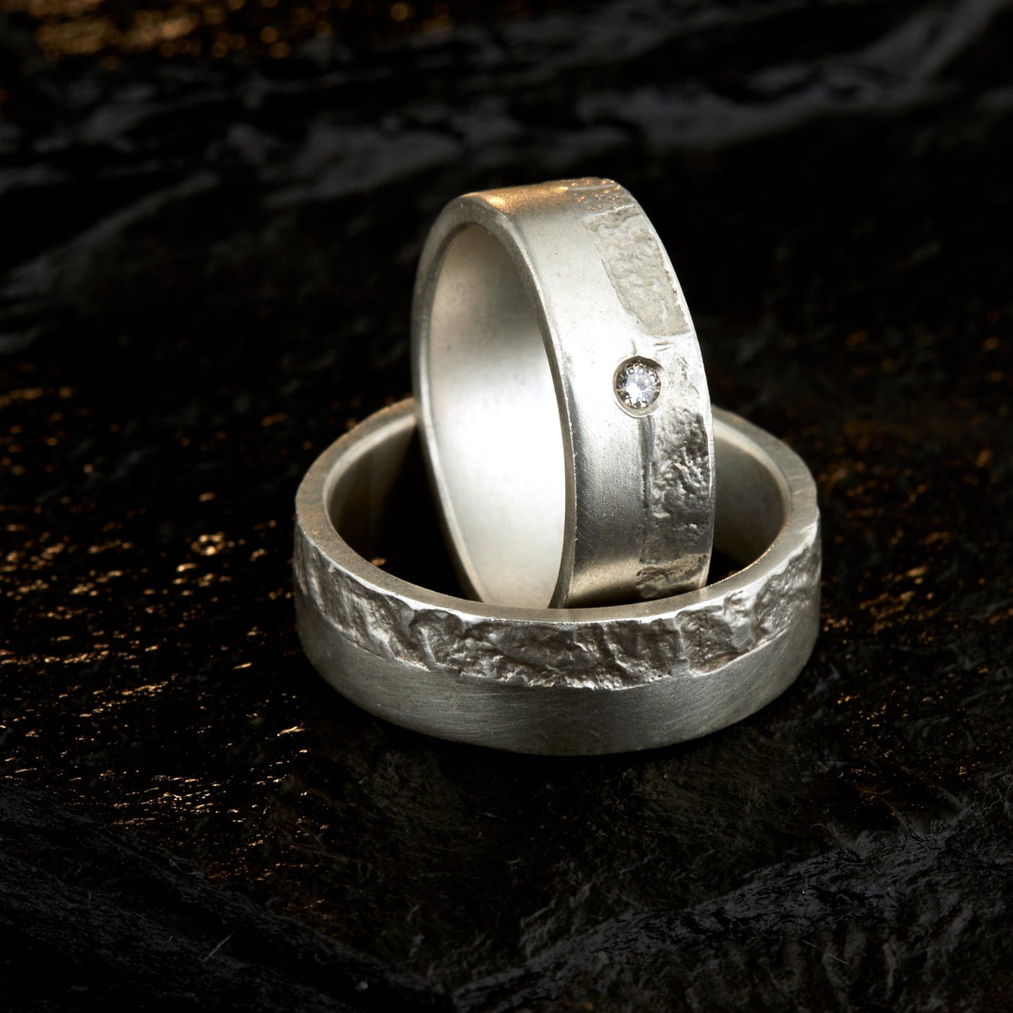 Massive Trauringe aus 925 Silber handgefertigt. Eheringe mit markanter Schieferstruktur retikuliert im Kontrast zu mattierten Oberflächen. Damenring ca. 6mm breit mit einem bündig gefassten 2mm Brillanten (TW/si). Herrenring ca. 6mm breit, massiv und charakterstark. Einzigartiges Partnerring-Set mit organischer Textur, inspiriert von natürlichem Fels. Handgemacht in eigener Werkstatt in Deutschland, keine CNC-Massenware. Hochwertige Unikate für Individualisten