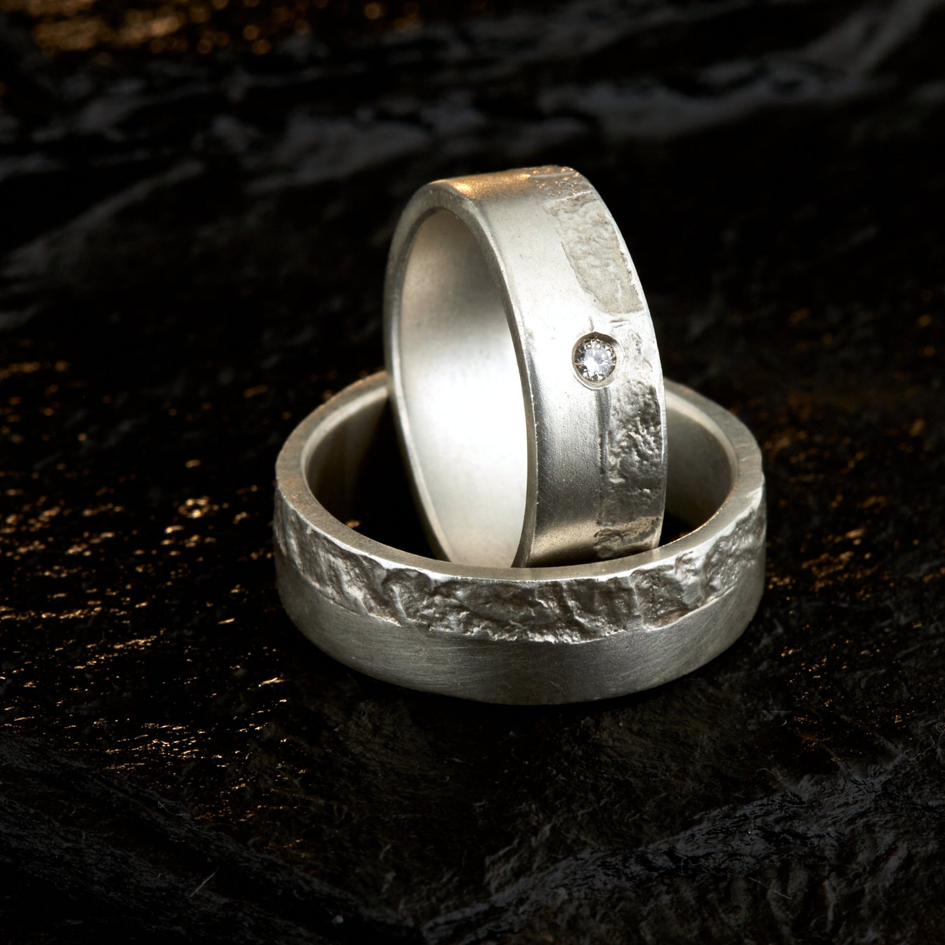 Massive Trauringe aus 925 Silber handgefertigt. Eheringe mit markanter Schieferstruktur retikuliert im Kontrast zu mattierten Oberflächen. Damenring ca. 6mm breit mit einem bündig gefassten 2mm Brillanten (TW/si). Herrenring ca. 6mm breit, massiv und charakterstark. Einzigartiges Partnerring-Set mit organischer Textur, inspiriert von natürlichem Fels. Handgemacht in eigener Werkstatt in Deutschland, keine CNC-Massenware. Hochwertige Unikate für Individualisten