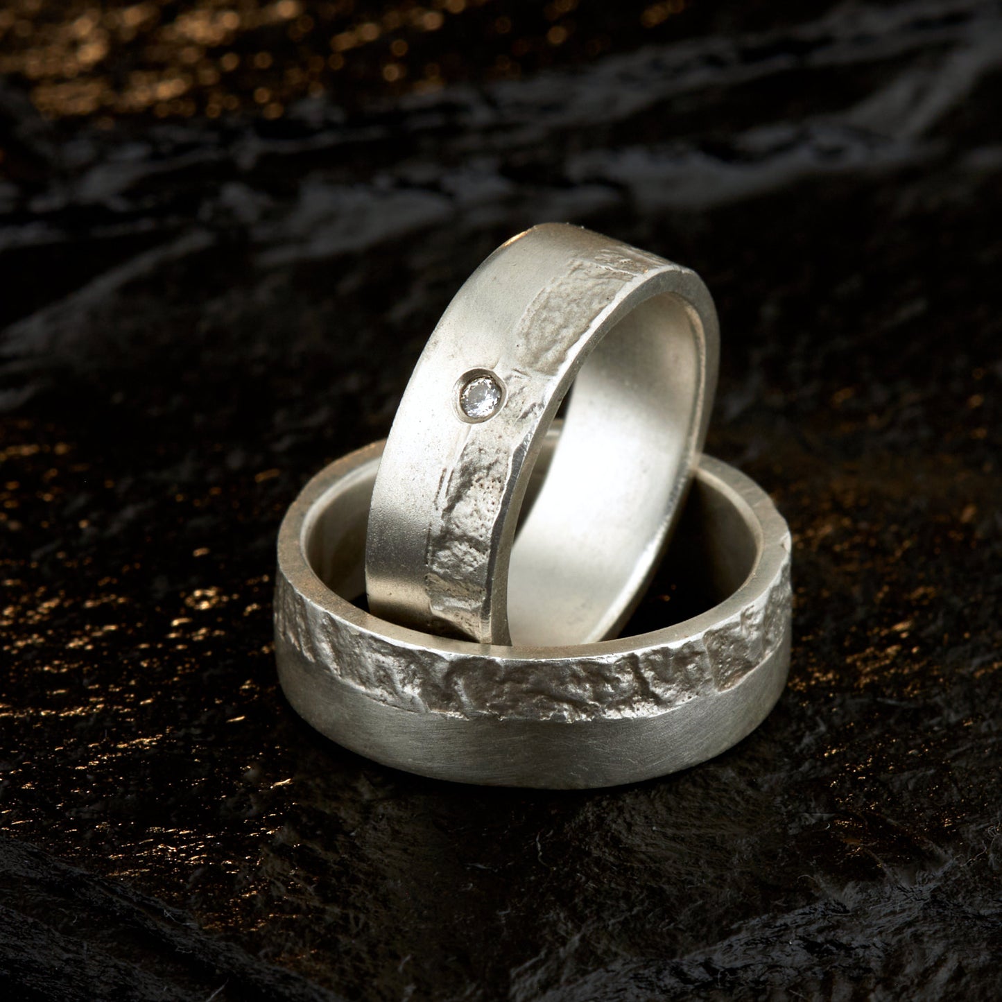 Massive Trauringe aus 925 Silber handgefertigt. Eheringe mit markanter Schieferstruktur retikuliert im Kontrast zu mattierten Oberflächen. Damenring ca. 6mm breit mit einem bündig gefassten 2mm Brillanten (TW/si). Herrenring ca. 6mm breit, massiv und charakterstark. Einzigartiges Partnerring-Set mit organischer Textur, inspiriert von natürlichem Fels. Handgemacht in eigener Werkstatt in Deutschland, keine CNC-Massenware. Hochwertige Unikate für Individualisten