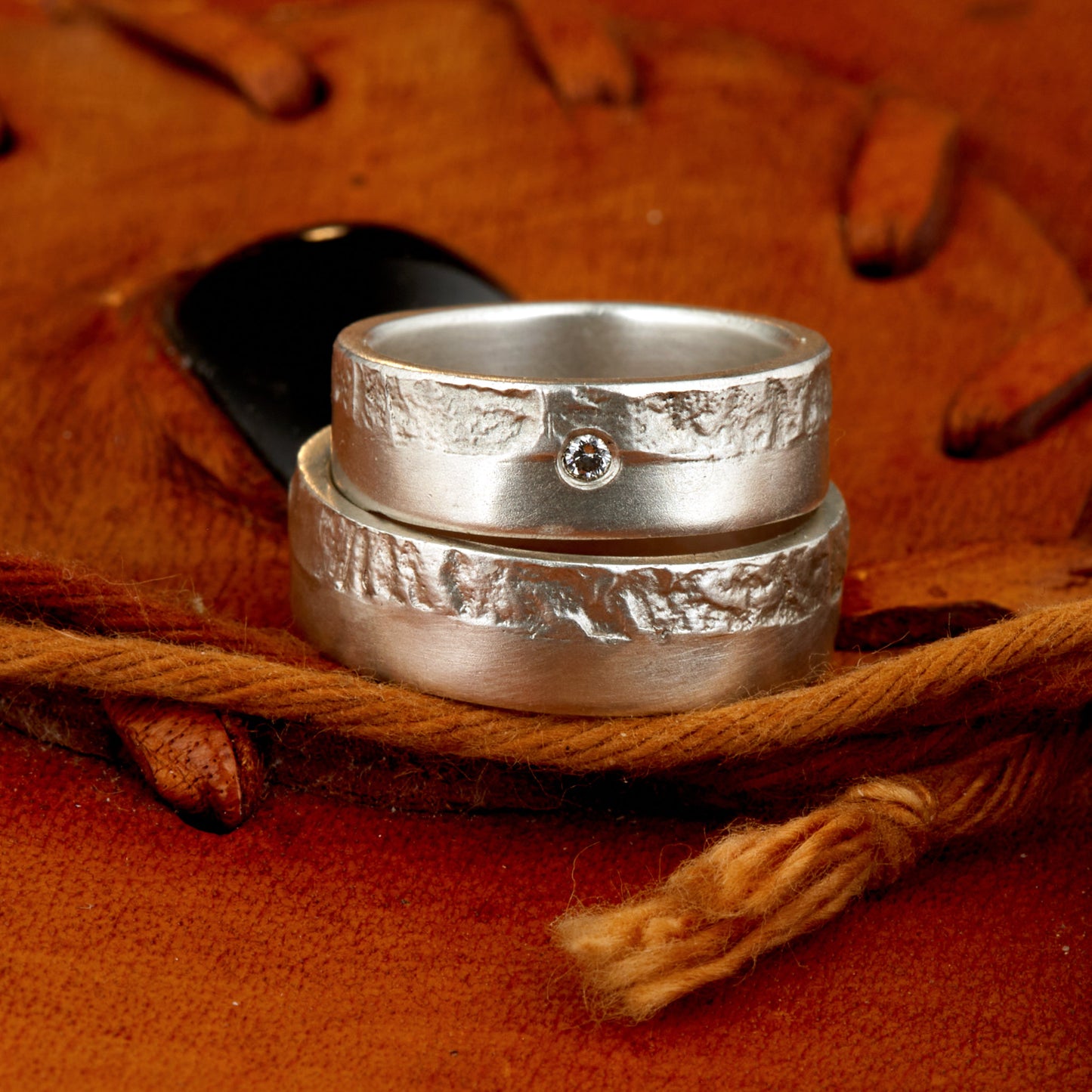 Massive Trauringe aus 925 Silber handgefertigt. Eheringe mit markanter Schieferstruktur retikuliert im Kontrast zu mattierten Oberflächen. Damenring ca. 6mm breit mit einem bündig gefassten 2mm Brillanten (TW/si). Herrenring ca. 6mm breit, massiv und charakterstark. Einzigartiges Partnerring-Set mit organischer Textur, inspiriert von natürlichem Fels. Handgemacht in eigener Werkstatt in Deutschland, keine CNC-Massenware. Hochwertige Unikate für Individualisten