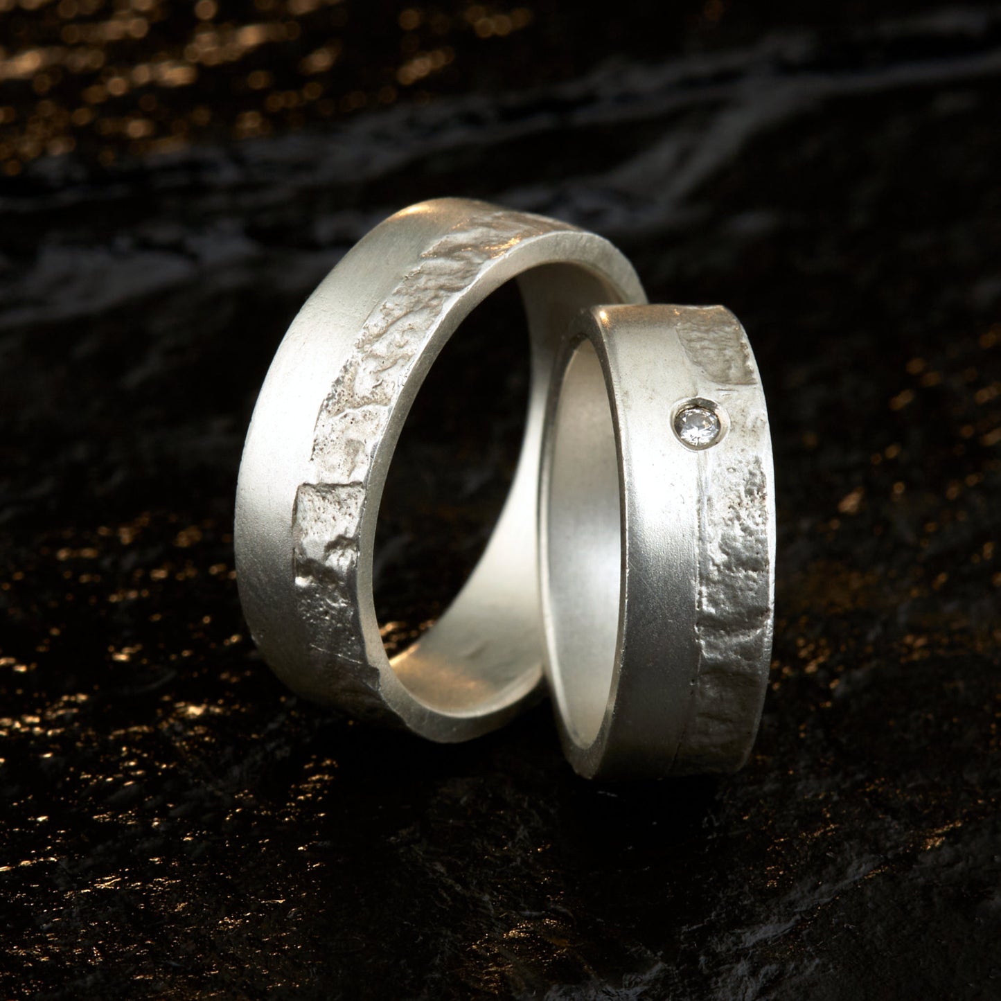 Massive Trauringe aus 925 Silber handgefertigt. Eheringe mit markanter Schieferstruktur retikuliert im Kontrast zu mattierten Oberflächen. Damenring ca. 6mm breit mit einem bündig gefassten 2mm Brillanten (TW/si). Herrenring ca. 6mm breit, massiv und charakterstark. Einzigartiges Partnerring-Set mit organischer Textur, inspiriert von natürlichem Fels. Handgemacht in eigener Werkstatt in Deutschland, keine CNC-Massenware. Hochwertige Unikate für Individualisten