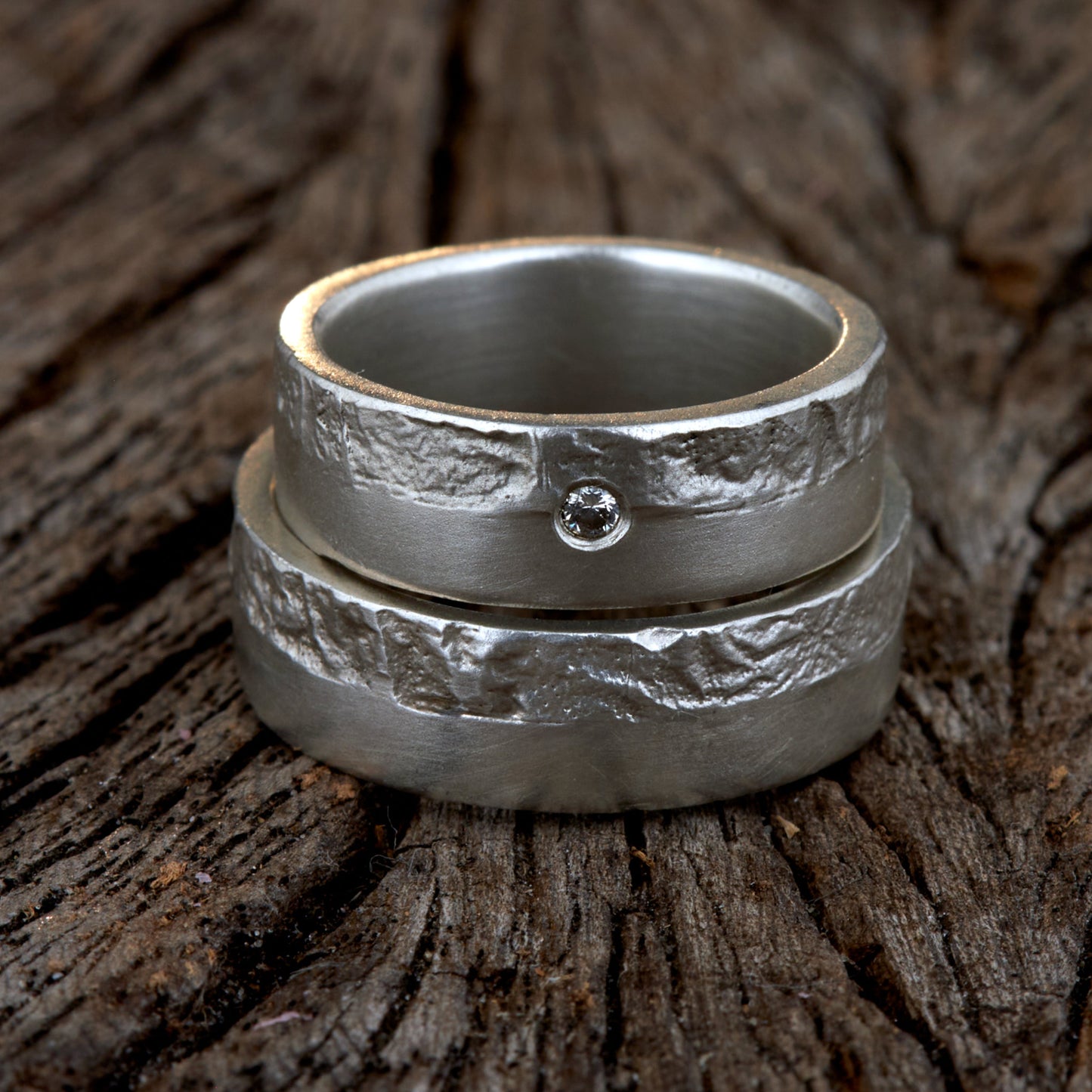 Massive Trauringe aus 925 Silber handgefertigt. Eheringe mit markanter Schieferstruktur retikuliert im Kontrast zu mattierten Oberflächen. Damenring ca. 6mm breit mit einem bündig gefassten 2mm Brillanten (TW/si). Herrenring ca. 6mm breit, massiv und charakterstark. Einzigartiges Partnerring-Set mit organischer Textur, inspiriert von natürlichem Fels. Handgemacht in eigener Werkstatt in Deutschland, keine CNC-Massenware. Hochwertige Unikate für Individualisten