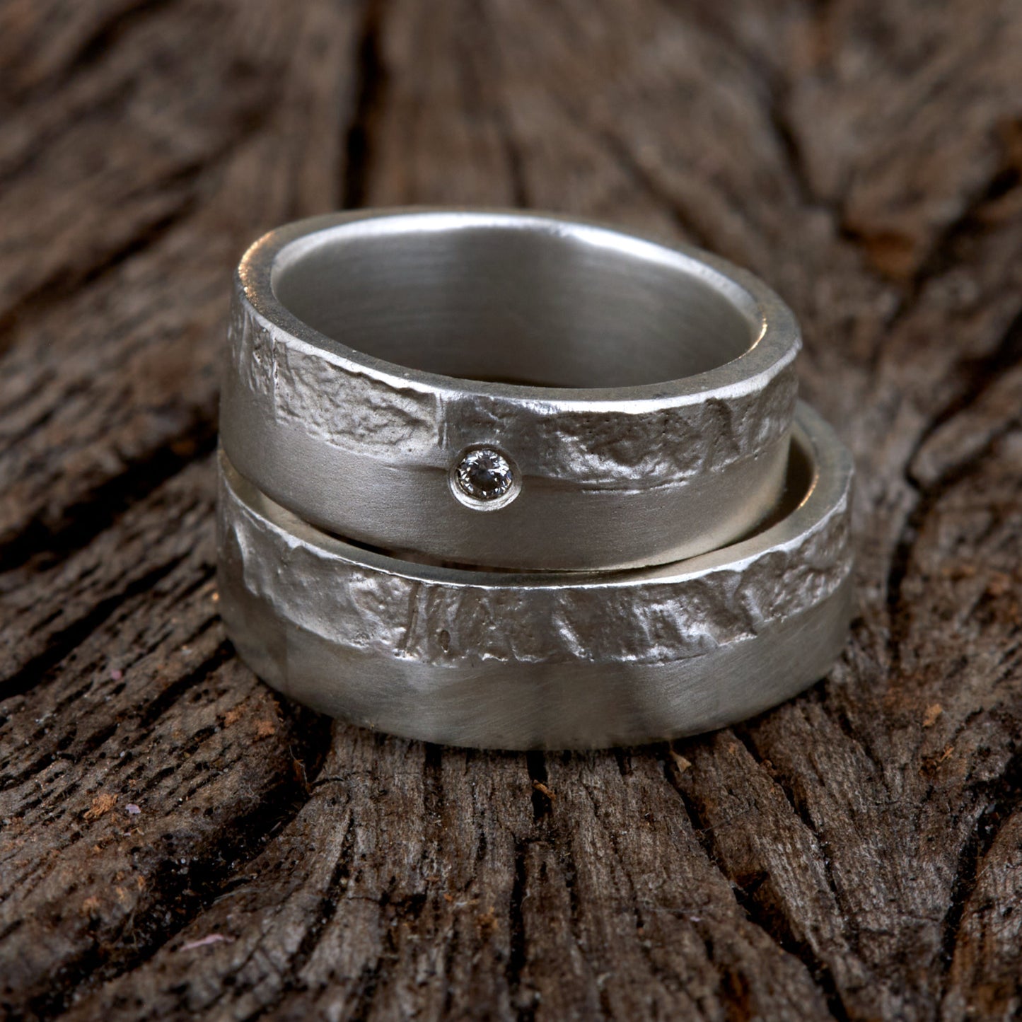 Massive Trauringe aus 925 Silber handgefertigt. Eheringe mit markanter Schieferstruktur retikuliert im Kontrast zu mattierten Oberflächen. Damenring ca. 6mm breit mit einem bündig gefassten 2mm Brillanten (TW/si). Herrenring ca. 6mm breit, massiv und charakterstark. Einzigartiges Partnerring-Set mit organischer Textur, inspiriert von natürlichem Fels. Handgemacht in eigener Werkstatt in Deutschland, keine CNC-Massenware. Hochwertige Unikate für Individualisten