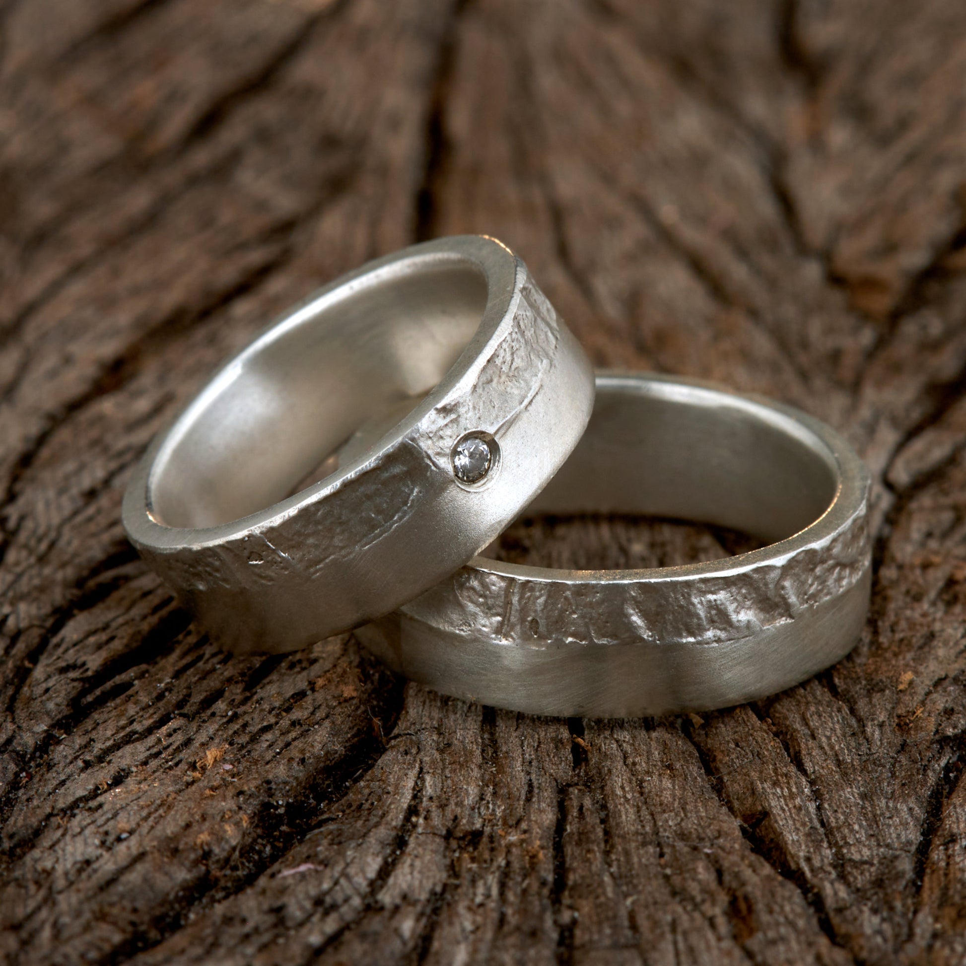 Massive Trauringe aus 925 Silber handgefertigt. Eheringe mit markanter Schieferstruktur retikuliert im Kontrast zu mattierten Oberflächen. Damenring ca. 6mm breit mit einem bündig gefassten 2mm Brillanten (TW/si). Herrenring ca. 6mm breit, massiv und charakterstark. Einzigartiges Partnerring-Set mit organischer Textur, inspiriert von natürlichem Fels. Handgemacht in eigener Werkstatt in Deutschland, keine CNC-Massenware. Hochwertige Unikate für Individualisten