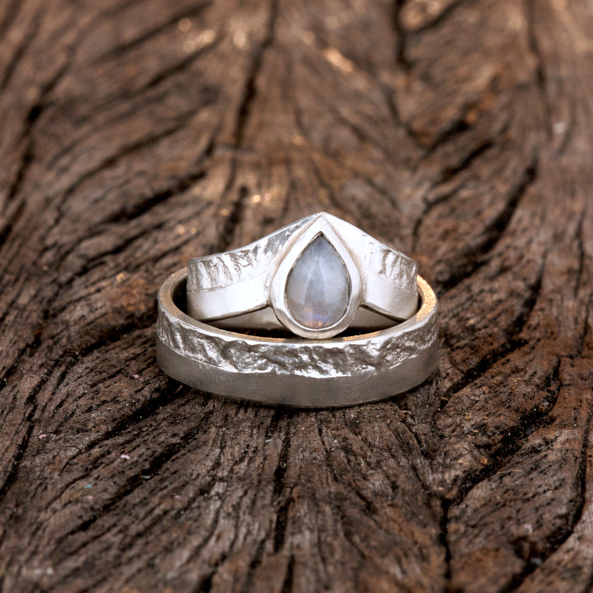 Hochwertiges Eheringe Set aus massivem 925 Sterling Silber mit kontrastreicher Oberfläche halb matt und halb retikuliert. Der Damenring in eleganter Wishbone V-Form trägt einen handgefassten Regenbogen-Mondstein im Tropfenschliff 9x6 mm mit blauem Schimmer. Der Herrenring ist 6x2 mm breit und spiegelt das maritime nordische Design wider. Handgefertigte Markenware aus der Goldschmiede Silberschweif für Paare die exklusiven Edelsteinschmuck und archaische Strukturen suchen