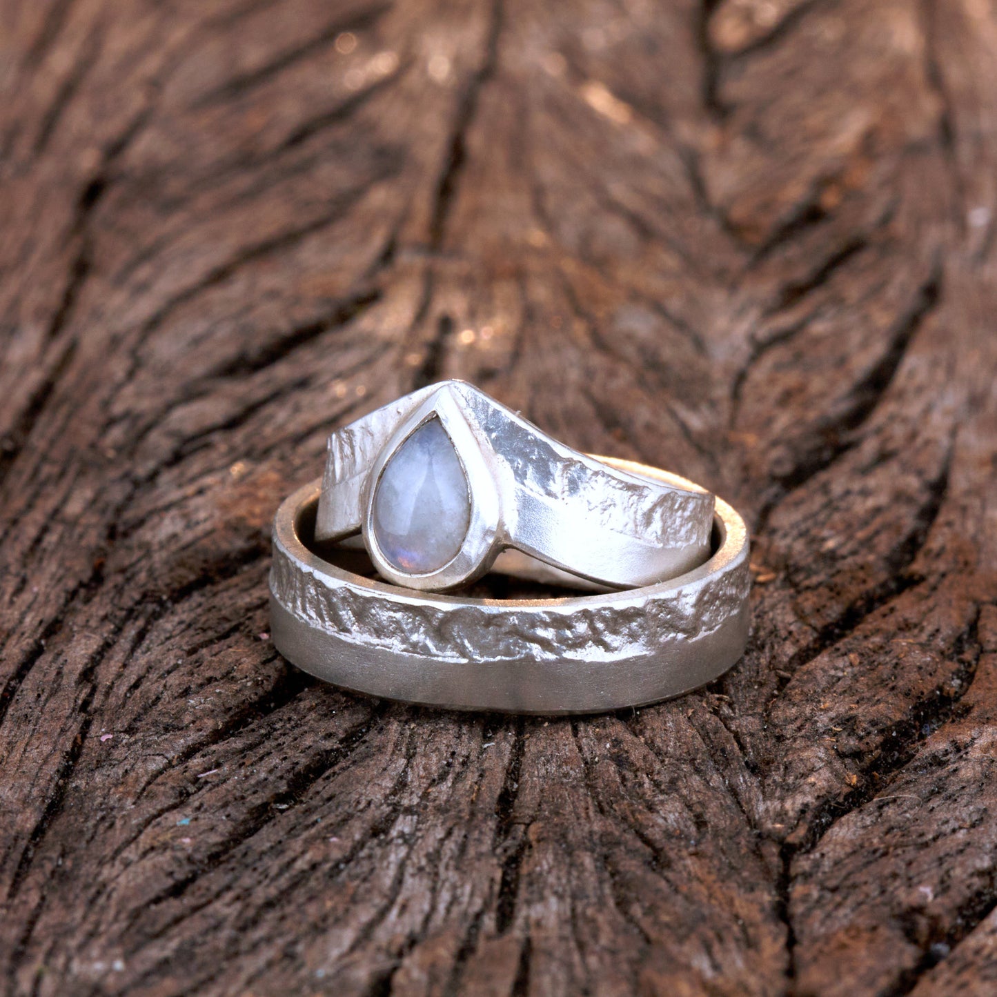 Hochwertiges Eheringe Set aus massivem 925 Sterling Silber mit kontrastreicher Oberfläche halb matt und halb retikuliert. Der Damenring in eleganter Wishbone V-Form trägt einen handgefassten Regenbogen-Mondstein im Tropfenschliff 9x6 mm mit blauem Schimmer. Der Herrenring ist 6x2 mm breit und spiegelt das maritime nordische Design wider. Handgefertigte Markenware aus der Goldschmiede Silberschweif für Paare die exklusiven Edelsteinschmuck und archaische Strukturen suchen