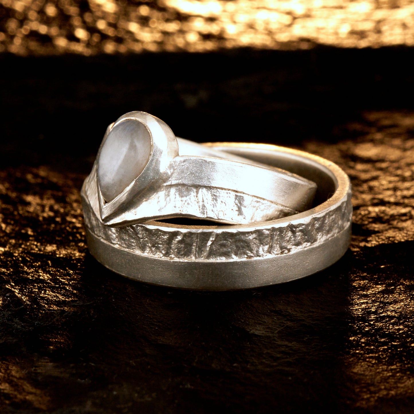 Hochwertiges Eheringe Set aus massivem 925 Sterling Silber mit kontrastreicher Oberfläche halb matt und halb retikuliert. Der Damenring in eleganter Wishbone V-Form trägt einen handgefassten Regenbogen-Mondstein im Tropfenschliff 9x6 mm mit blauem Schimmer. Der Herrenring ist 6x2 mm breit und spiegelt das maritime nordische Design wider. Handgefertigte Markenware aus der Goldschmiede Silberschweif für Paare die exklusiven Edelsteinschmuck und archaische Strukturen suchen