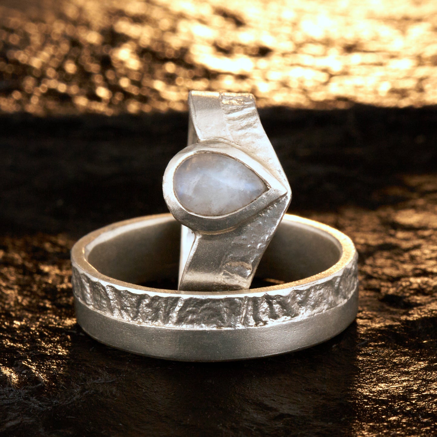 Hochwertiges Eheringe Set aus massivem 925 Sterling Silber mit kontrastreicher Oberfläche halb matt und halb retikuliert. Der Damenring in eleganter Wishbone V-Form trägt einen handgefassten Regenbogen-Mondstein im Tropfenschliff 9x6 mm mit blauem Schimmer. Der Herrenring ist 6x2 mm breit und spiegelt das maritime nordische Design wider. Handgefertigte Markenware aus der Goldschmiede Silberschweif für Paare die exklusiven Edelsteinschmuck und archaische Strukturen suchen