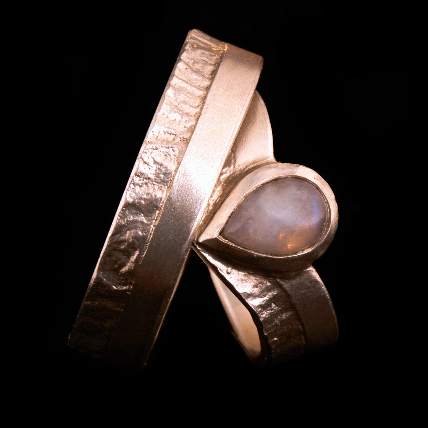 Hochwertiges Eheringe Set aus massivem 925 Sterling Silber mit kontrastreicher Oberfläche halb matt und halb retikuliert. Der Damenring in eleganter Wishbone V-Form trägt einen handgefassten Regenbogen-Mondstein im Tropfenschliff 9x6 mm mit blauem Schimmer. Der Herrenring ist 6x2 mm breit und spiegelt das maritime nordische Design wider. Handgefertigte Markenware aus der Goldschmiede Silberschweif für Paare die exklusiven Edelsteinschmuck und archaische Strukturen suchen