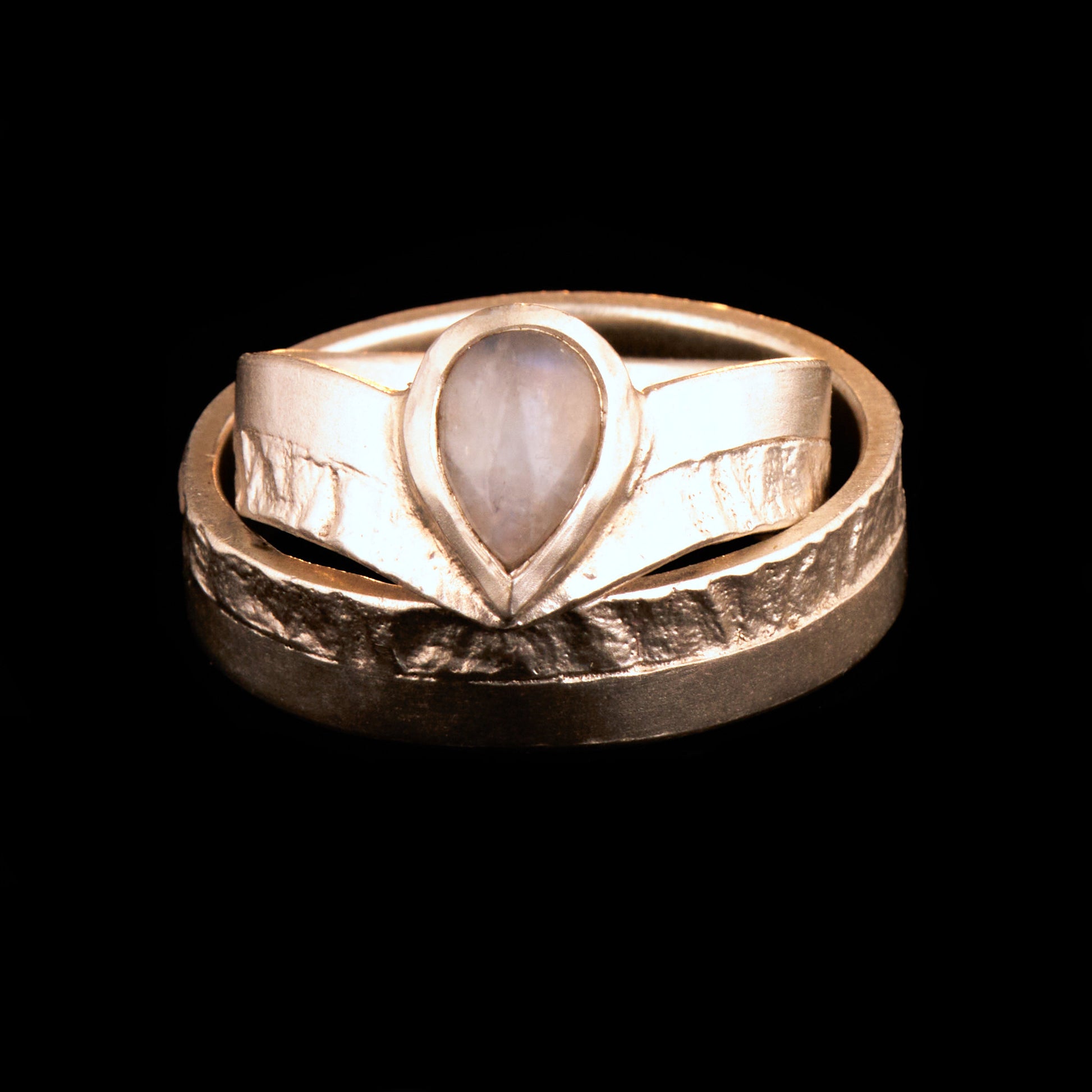 Hochwertiges Eheringe Set aus massivem 925 Sterling Silber mit kontrastreicher Oberfläche halb matt und halb retikuliert. Der Damenring in eleganter Wishbone V-Form trägt einen handgefassten Regenbogen-Mondstein im Tropfenschliff 9x6 mm mit blauem Schimmer. Der Herrenring ist 6x2 mm breit und spiegelt das maritime nordische Design wider. Handgefertigte Markenware aus der Goldschmiede Silberschweif für Paare die exklusiven Edelsteinschmuck und archaische Strukturen suchen