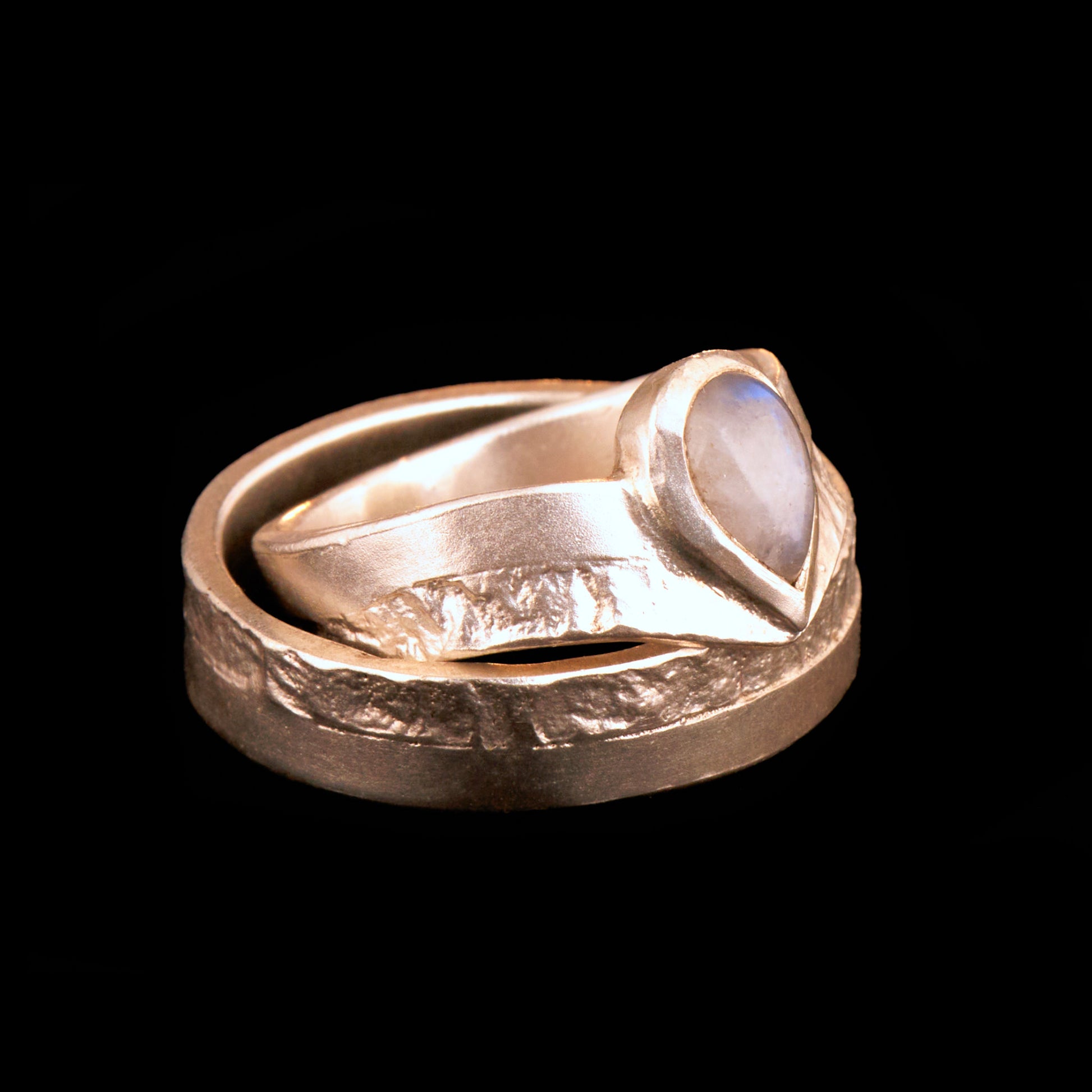 Hochwertiges Eheringe Set aus massivem 925 Sterling Silber mit kontrastreicher Oberfläche halb matt und halb retikuliert. Der Damenring in eleganter Wishbone V-Form trägt einen handgefassten Regenbogen-Mondstein im Tropfenschliff 9x6 mm mit blauem Schimmer. Der Herrenring ist 6x2 mm breit und spiegelt das maritime nordische Design wider. Handgefertigte Markenware aus der Goldschmiede Silberschweif für Paare die exklusiven Edelsteinschmuck und archaische Strukturen suchen