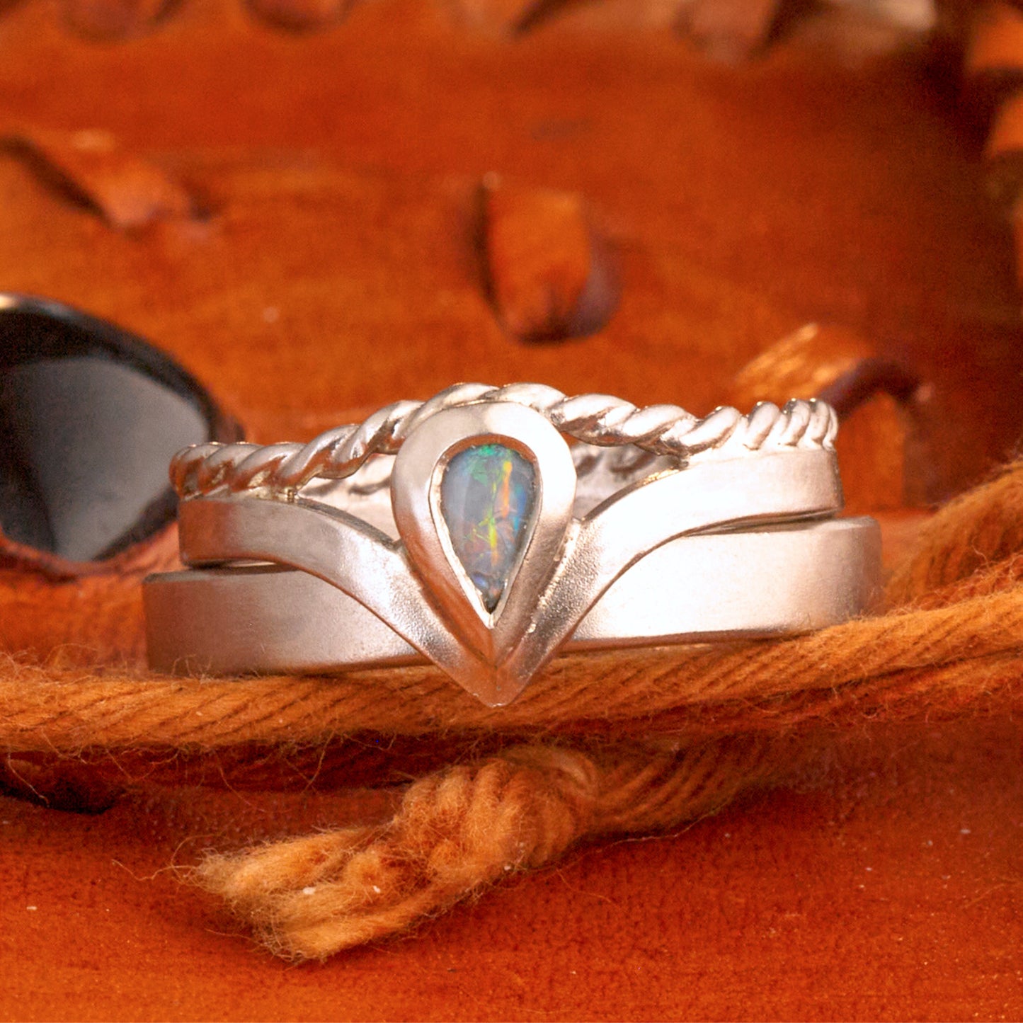 Damenring Detail: Handgefertigter Wishbone-Ring aus mattem 925 Silber von Silberschweif mit einem 6x4 mm Opaltropfen. Man erkennt das detailreiche Kordeldesign und die präzise Fassung des Edelsteins.
Set-Ansicht: Minimalistisches Trauring-Set aus Silber. Der filigrane Damenring mit Opal und Kordelschiene liegt auf dem schlichten, 4 mm breiten Herrenring vor einem rustikalen Steinhintergrund.
Herrenring Fokus: Schlichter silberner Herrenring (4x2 mm) mit matter Oberfläche, handgefertigt in Deutschland. 