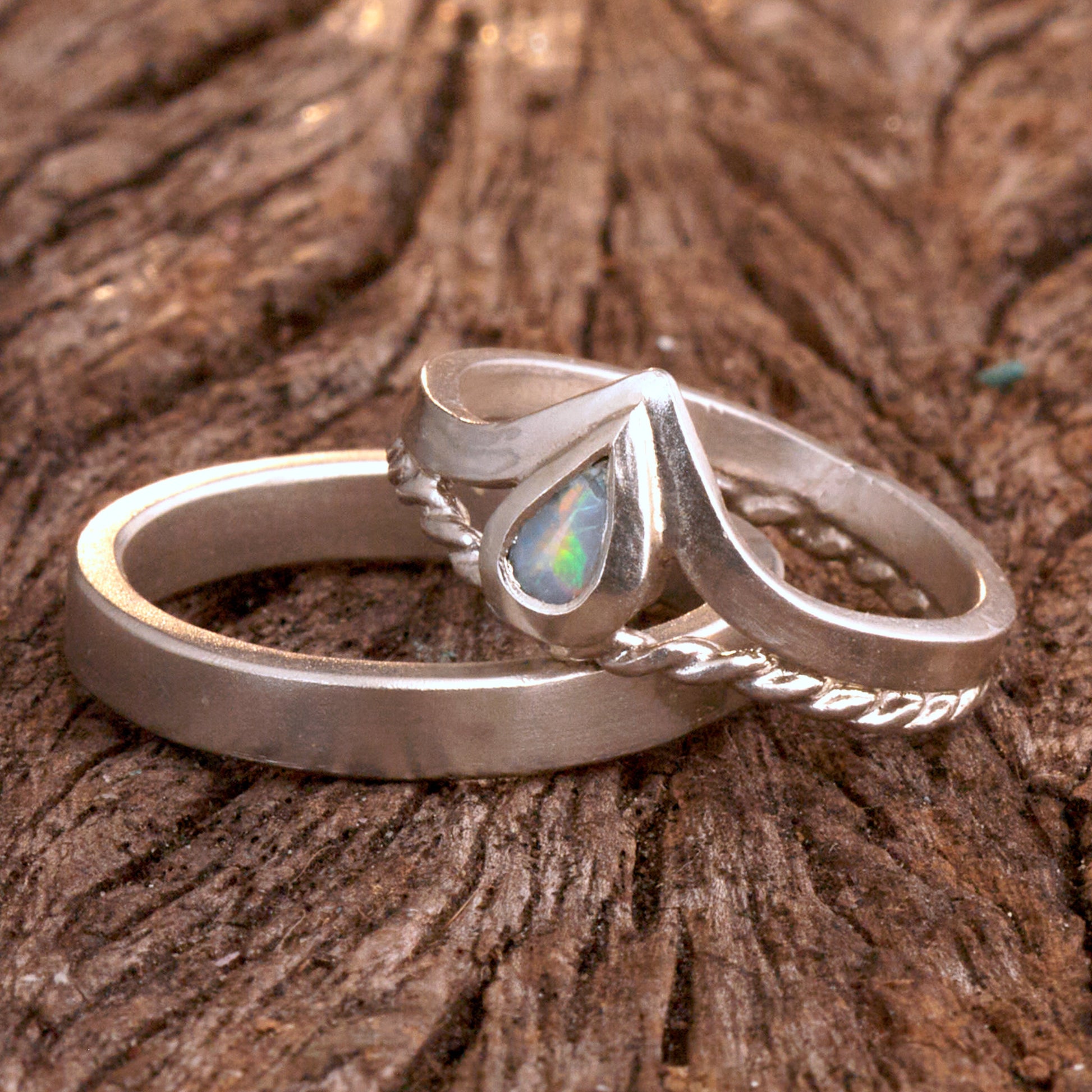 Damenring Detail: Handgefertigter Wishbone-Ring aus mattem 925 Silber von Silberschweif mit einem 6x4 mm Opaltropfen. Man erkennt das detailreiche Kordeldesign und die präzise Fassung des Edelsteins.
Set-Ansicht: Minimalistisches Trauring-Set aus Silber. Der filigrane Damenring mit Opal und Kordelschiene liegt auf dem schlichten, 4 mm breiten Herrenring vor einem rustikalen Steinhintergrund.
Herrenring Fokus: Schlichter silberner Herrenring (4x2 mm) mit matter Oberfläche, handgefertigt in Deutschland. 