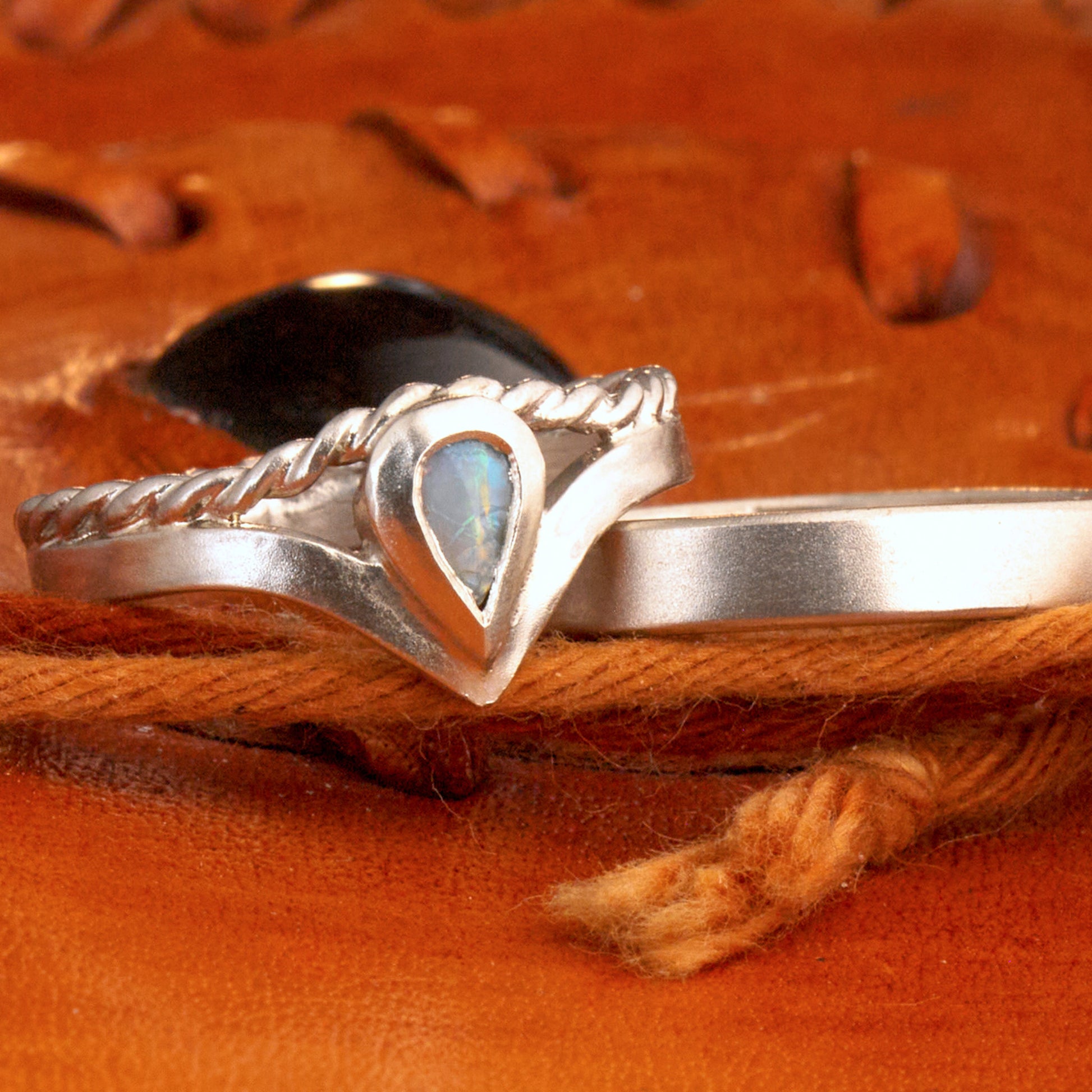 Damenring Detail: Handgefertigter Wishbone-Ring aus mattem 925 Silber von Silberschweif mit einem 6x4 mm Opaltropfen. Man erkennt das detailreiche Kordeldesign und die präzise Fassung des Edelsteins.
Set-Ansicht: Minimalistisches Trauring-Set aus Silber. Der filigrane Damenring mit Opal und Kordelschiene liegt auf dem schlichten, 4 mm breiten Herrenring vor einem rustikalen Steinhintergrund.
Herrenring Fokus: Schlichter silberner Herrenring (4x2 mm) mit matter Oberfläche, handgefertigt in Deutschland. 