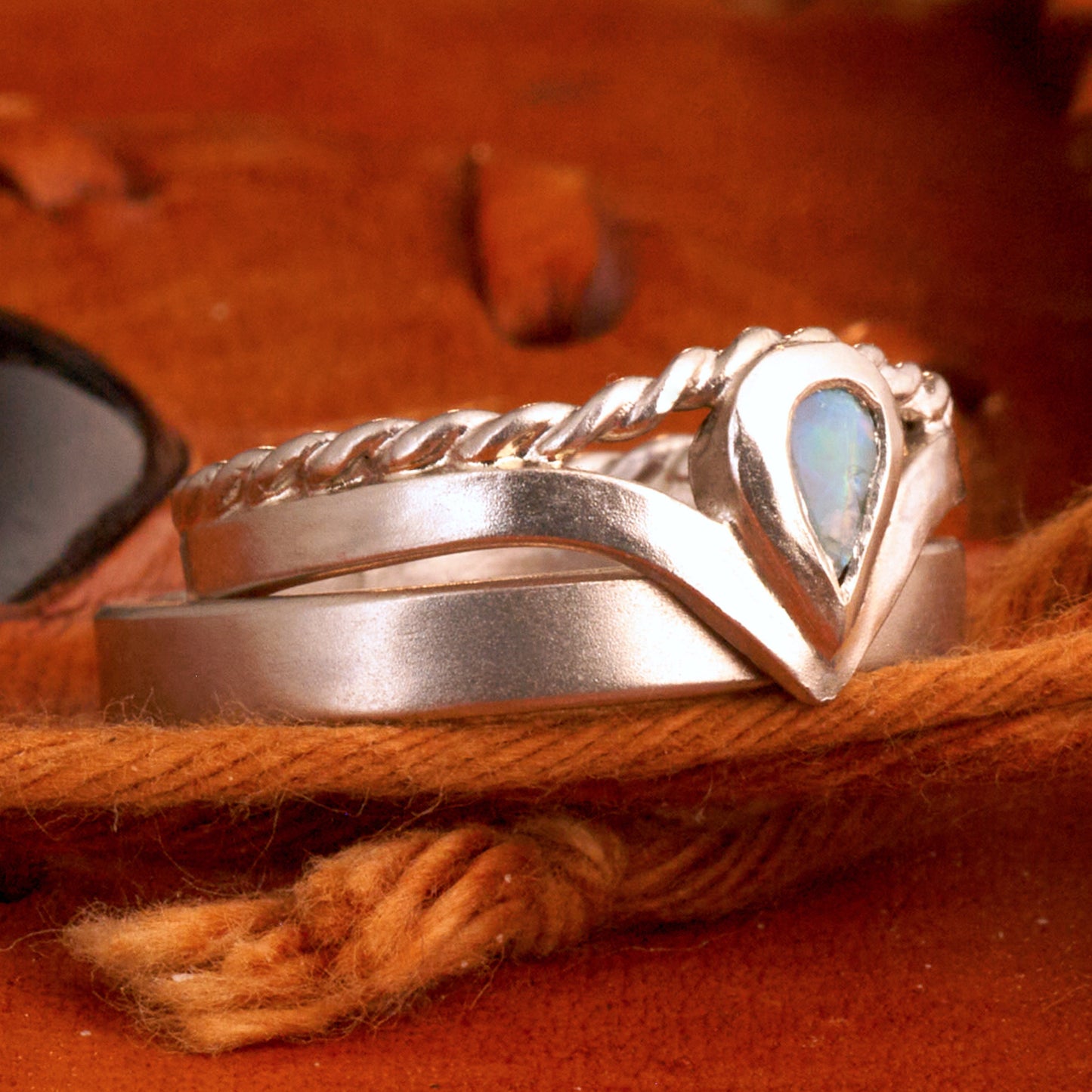 Damenring Detail: Handgefertigter Wishbone-Ring aus mattem 925 Silber von Silberschweif mit einem 6x4 mm Opaltropfen. Man erkennt das detailreiche Kordeldesign und die präzise Fassung des Edelsteins.
Set-Ansicht: Minimalistisches Trauring-Set aus Silber. Der filigrane Damenring mit Opal und Kordelschiene liegt auf dem schlichten, 4 mm breiten Herrenring vor einem rustikalen Steinhintergrund.
Herrenring Fokus: Schlichter silberner Herrenring (4x2 mm) mit matter Oberfläche, handgefertigt in Deutschland. 