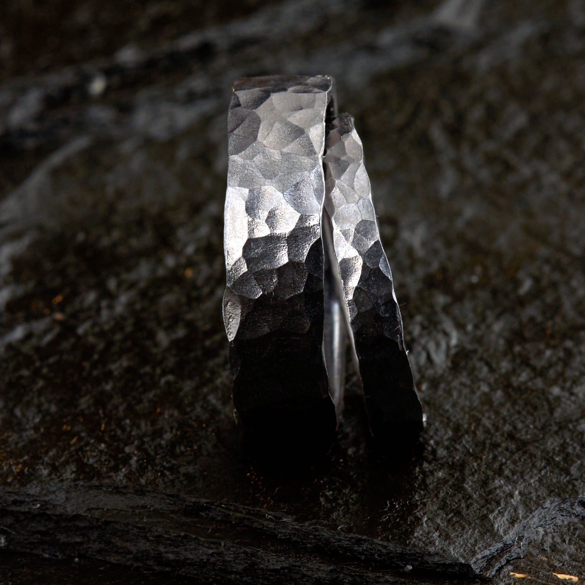 Handgefertigtes Ehering-Set aus massivem Tantal auf rustikalem Leder. Herrenring (6mm) und Damenring (4mm) mit markanter, gehämmerter Oberfläche in dunklem Anthrazit. Einzigartige Schmiedekunst für exklusive Hochzeitsringe. SEO-Keywords: Tantal Eheringe gehämmert, dunkle Trauringe, Tantalum Wedding Bands, nachhaltiger Luxusschmuck, seltene Edelmetalle Hochzeit. Sichtbare Details der individuellen Textur und des tiefen, metallischen Glanzes.