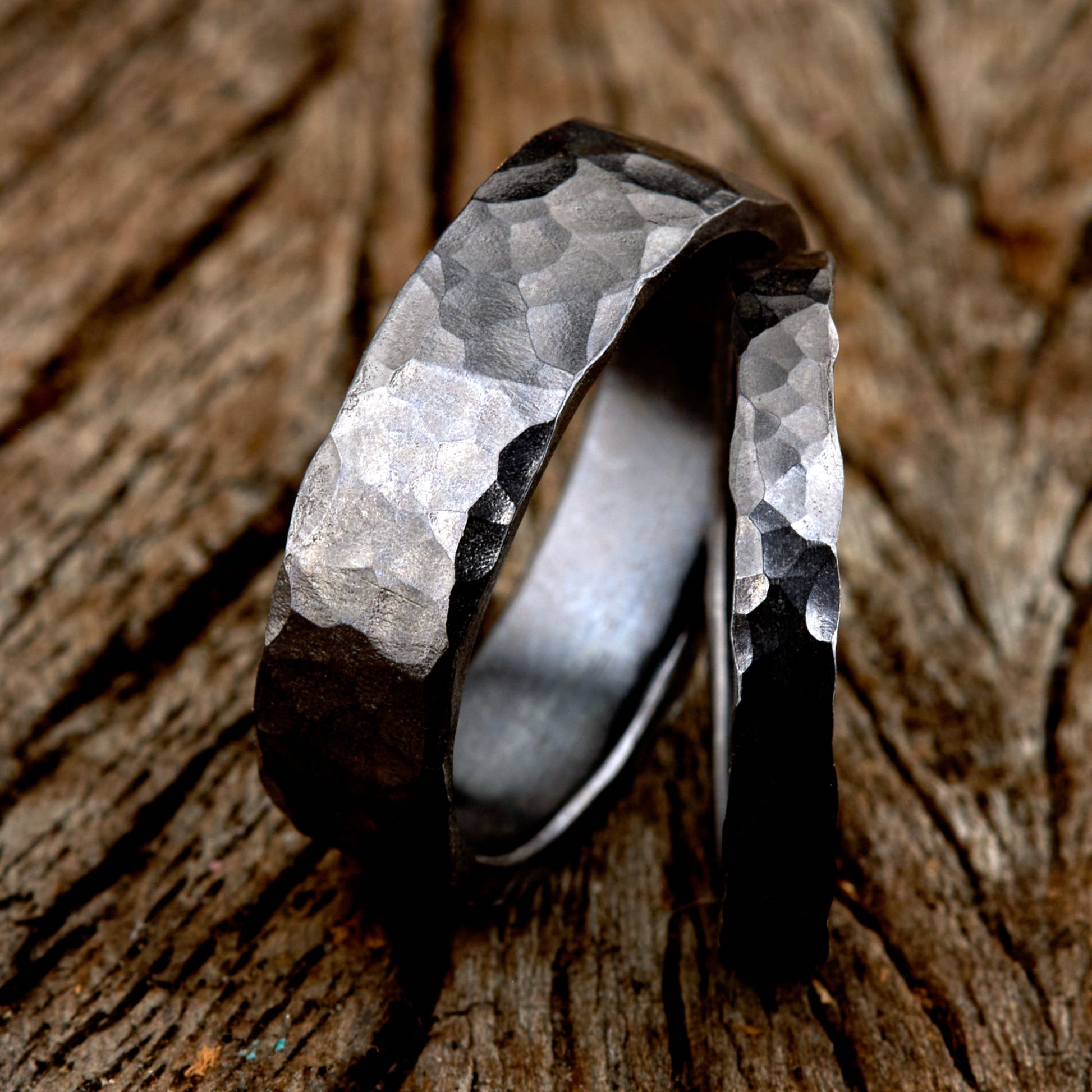 Handgefertigtes Ehering-Set aus massivem Tantal auf rustikalem Leder. Herrenring (6mm) und Damenring (4mm) mit markanter, gehämmerter Oberfläche in dunklem Anthrazit. Einzigartige Schmiedekunst für exklusive Hochzeitsringe. SEO-Keywords: Tantal Eheringe gehämmert, dunkle Trauringe, Tantalum Wedding Bands, nachhaltiger Luxusschmuck, seltene Edelmetalle Hochzeit. Sichtbare Details der individuellen Textur und des tiefen, metallischen Glanzes.