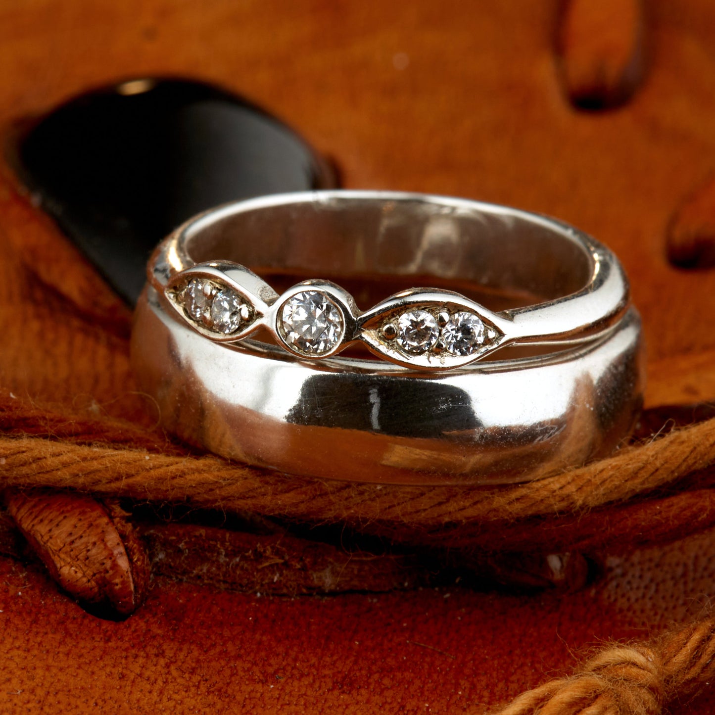 Exklusives Ehering-Set aus 925 Silber auf braunem Leder. Damenring (4mm) mit 5 handgefassten Moissaniten (1x 3mm, 4x 2mm) für maximale Lichtreflexion. Massiver Herrenring (6mm breit, 2mm stark) in Hochglanz-Optik. Nachhaltige Trauringe als ethische Alternative zum Diamanten. SEO-Keywords: Moissanit Trauringe Silber, handgefertigte Hochzeitsringe Set, nachhaltiger Schmuck, 925 Silber Ringe mit Moissanit, Eheringe Set günstig Luxus.