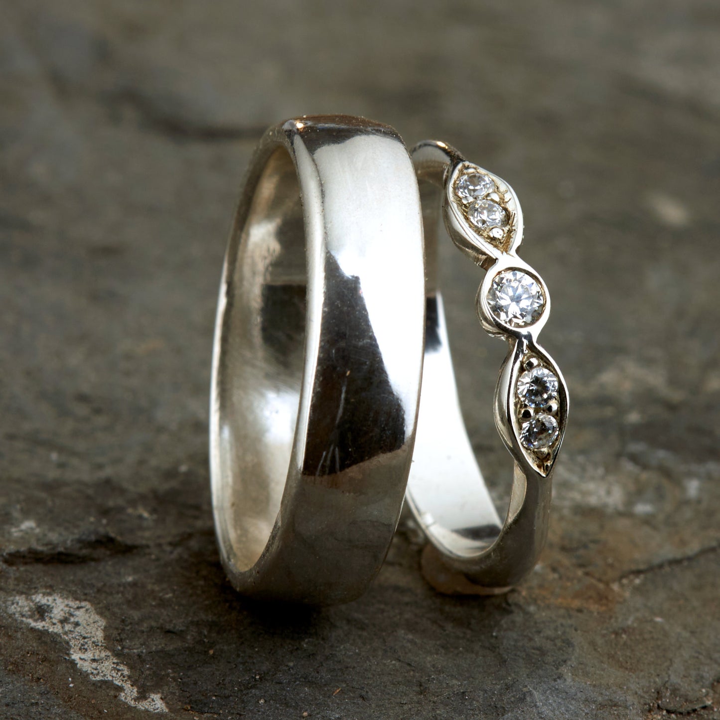 Exklusives Ehering-Set aus 925 Silber auf braunem Leder. Damenring (4mm) mit 5 handgefassten Moissaniten (1x 3mm, 4x 2mm) für maximale Lichtreflexion. Massiver Herrenring (6mm breit, 2mm stark) in Hochglanz-Optik. Nachhaltige Trauringe als ethische Alternative zum Diamanten. SEO-Keywords: Moissanit Trauringe Silber, handgefertigte Hochzeitsringe Set, nachhaltiger Schmuck, 925 Silber Ringe mit Moissanit, Eheringe Set günstig Luxus.