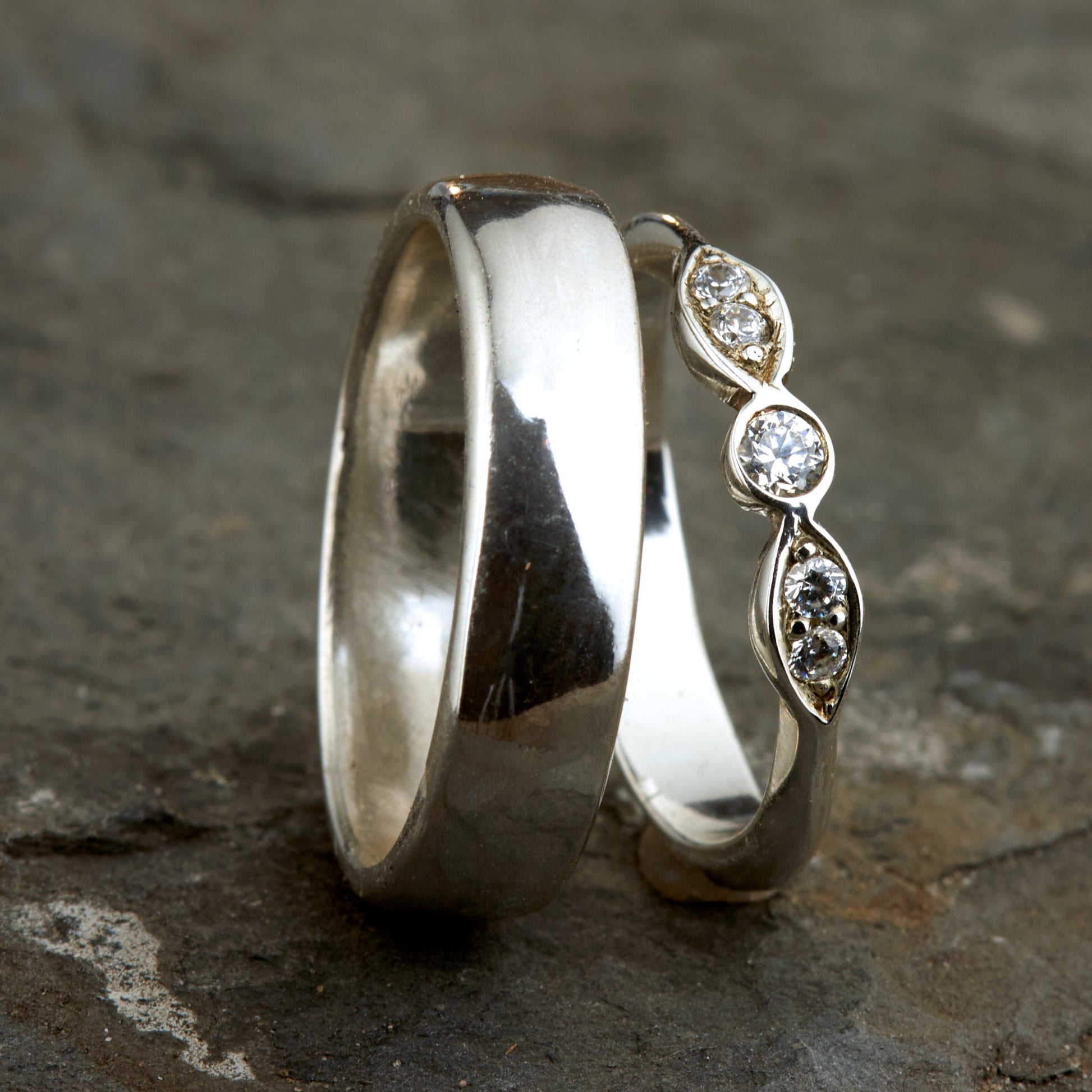 Exklusives Ehering-Set aus 925 Silber auf braunem Leder. Damenring (4mm) mit 5 handgefassten Moissaniten (1x 3mm, 4x 2mm) für maximale Lichtreflexion. Massiver Herrenring (6mm breit, 2mm stark) in Hochglanz-Optik. Nachhaltige Trauringe als ethische Alternative zum Diamanten. SEO-Keywords: Moissanit Trauringe Silber, handgefertigte Hochzeitsringe Set, nachhaltiger Schmuck, 925 Silber Ringe mit Moissanit, Eheringe Set günstig Luxus.