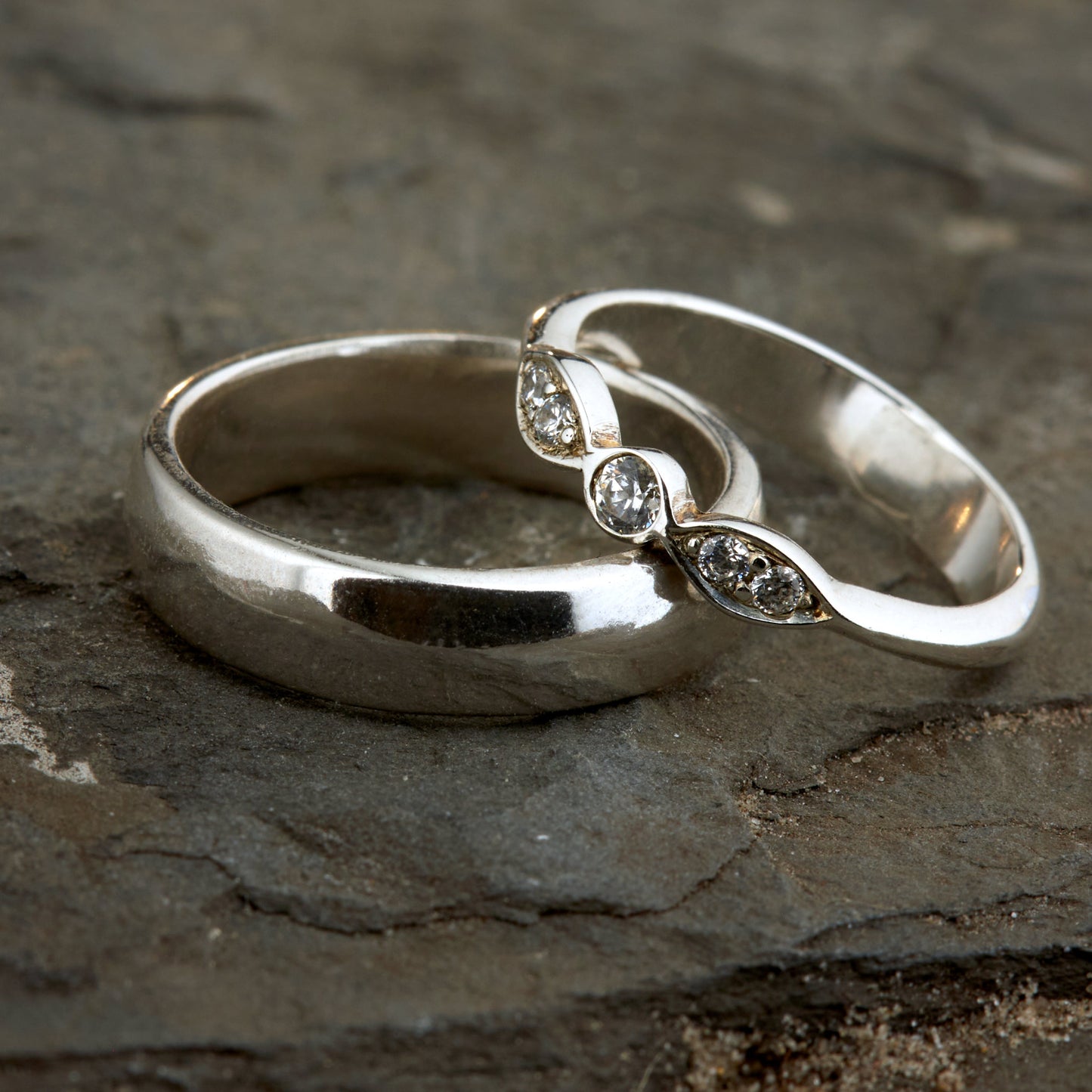 Exklusives Ehering-Set aus 925 Silber auf braunem Leder. Damenring (4mm) mit 5 handgefassten Moissaniten (1x 3mm, 4x 2mm) für maximale Lichtreflexion. Massiver Herrenring (6mm breit, 2mm stark) in Hochglanz-Optik. Nachhaltige Trauringe als ethische Alternative zum Diamanten. SEO-Keywords: Moissanit Trauringe Silber, handgefertigte Hochzeitsringe Set, nachhaltiger Schmuck, 925 Silber Ringe mit Moissanit, Eheringe Set günstig Luxus.