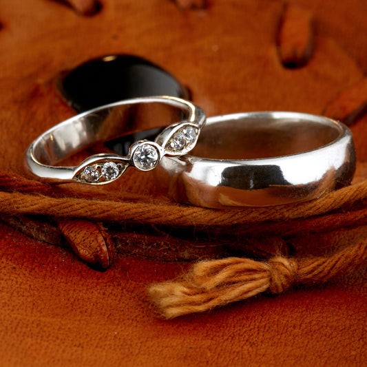 Exklusives Ehering-Set aus 925 Silber auf braunem Leder. Damenring (4mm) mit 5 handgefassten Moissaniten (1x 3mm, 4x 2mm) für maximale Lichtreflexion. Massiver Herrenring (6mm breit, 2mm stark) in Hochglanz-Optik. Nachhaltige Trauringe als ethische Alternative zum Diamanten. SEO-Keywords: Moissanit Trauringe Silber, handgefertigte Hochzeitsringe Set, nachhaltiger Schmuck, 925 Silber Ringe mit Moissanit, Eheringe Set günstig Luxus.