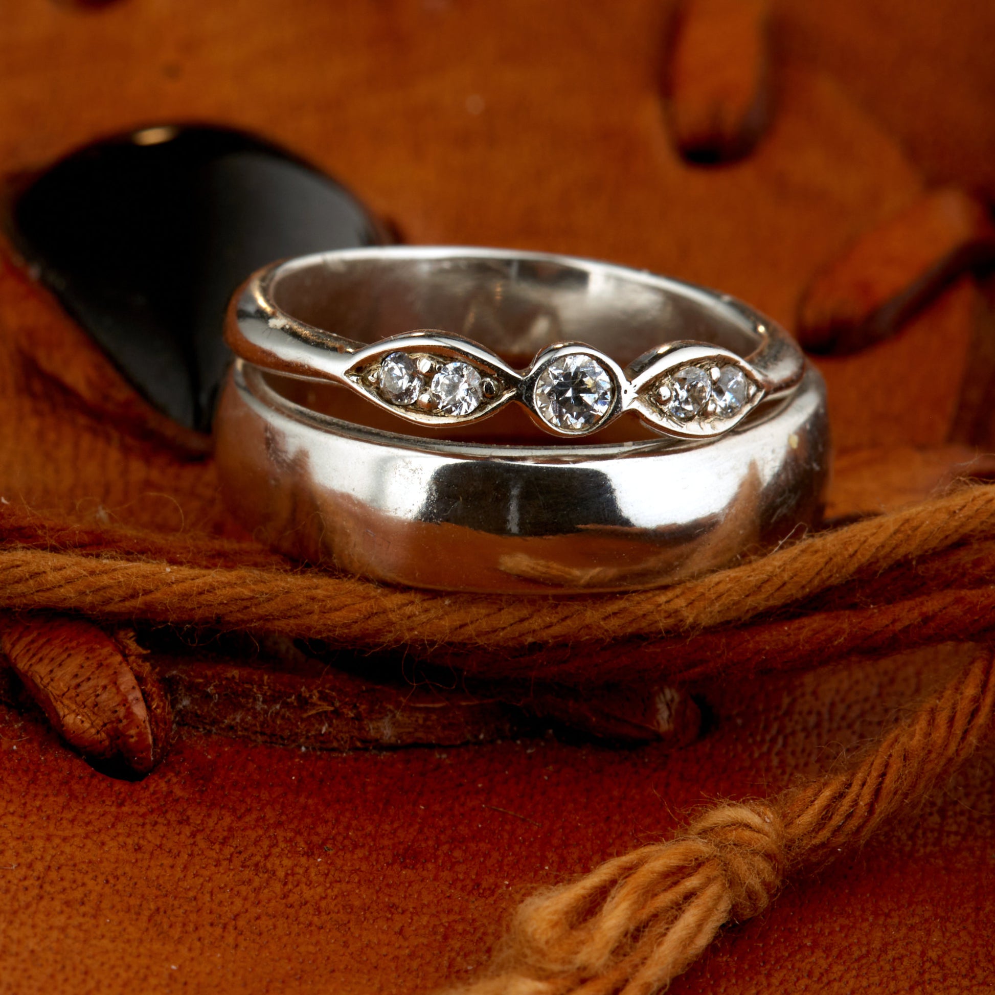 Exklusives Ehering-Set aus 925 Silber auf braunem Leder. Damenring (4mm) mit 5 handgefassten Moissaniten (1x 3mm, 4x 2mm) für maximale Lichtreflexion. Massiver Herrenring (6mm breit, 2mm stark) in Hochglanz-Optik. Nachhaltige Trauringe als ethische Alternative zum Diamanten. SEO-Keywords: Moissanit Trauringe Silber, handgefertigte Hochzeitsringe Set, nachhaltiger Schmuck, 925 Silber Ringe mit Moissanit, Eheringe Set günstig Luxus.