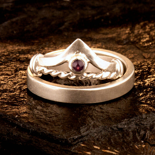 Handgefertigter Vintage Wishbone-Ring aus mattem 925 Silber mit einem violetten 3 mm Amethyst Cabochon in Zargenfassung. Man sieht deutlich die geteilte Schiene mit der filigranen Kordel-Verblendung.
Set-Präsentation: Minimalistisches Ehering-Set von Silberschweif auf dunklem Stein. Der verspielte Damenring mit lila Edelstein harmoniert perfekt mit dem schlichten, 4 mm breiten matten Herrenring.
Detail Ringschiene: Seitenansicht des Damenrings zeigt die handwerkliche Aufteilung der 4 mm Silberschiene 