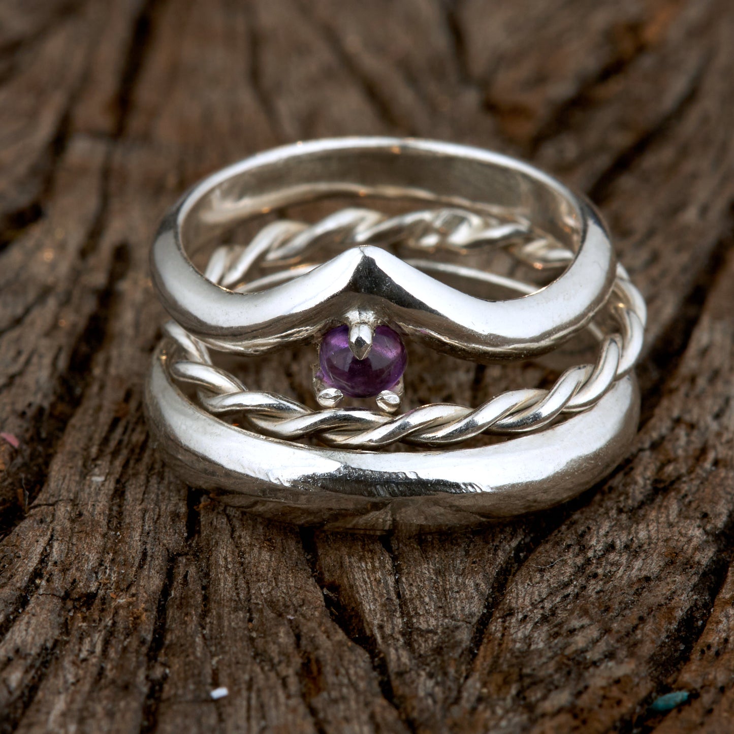Handgefertigtes Ehering-Set aus 925 Silber auf Leder. 3-teiliges Damen-Set bestehend aus einem 3mm Wishbone-Ring mit Amethyst und einem 2mm Kordelring. Daneben ein massiver 4mm Herrenring im Halbrund-Profil. Zeitloses Design mit lila Edelstein für die Hochzeit. SEO-Keywords: Wishbone Eheringe Silber, Amethyst Trauringe Set, handgefertigte Silberringe, 925 Sterlingsilber Schmuck, Kordelring Hochzeit. Sichtbare Details der hochwertigen Handarbeit und Steinbesetzung.