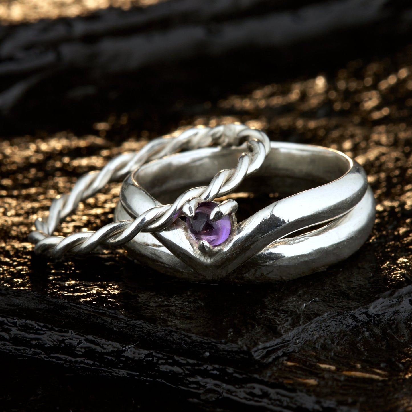 Handgefertigtes Ehering-Set aus 925 Silber auf Leder. 3-teiliges Damen-Set bestehend aus einem 3mm Wishbone-Ring mit Amethyst und einem 2mm Kordelring. Daneben ein massiver 4mm Herrenring im Halbrund-Profil. Zeitloses Design mit lila Edelstein für die Hochzeit. SEO-Keywords: Wishbone Eheringe Silber, Amethyst Trauringe Set, handgefertigte Silberringe, 925 Sterlingsilber Schmuck, Kordelring Hochzeit. Sichtbare Details der hochwertigen Handarbeit und Steinbesetzung.