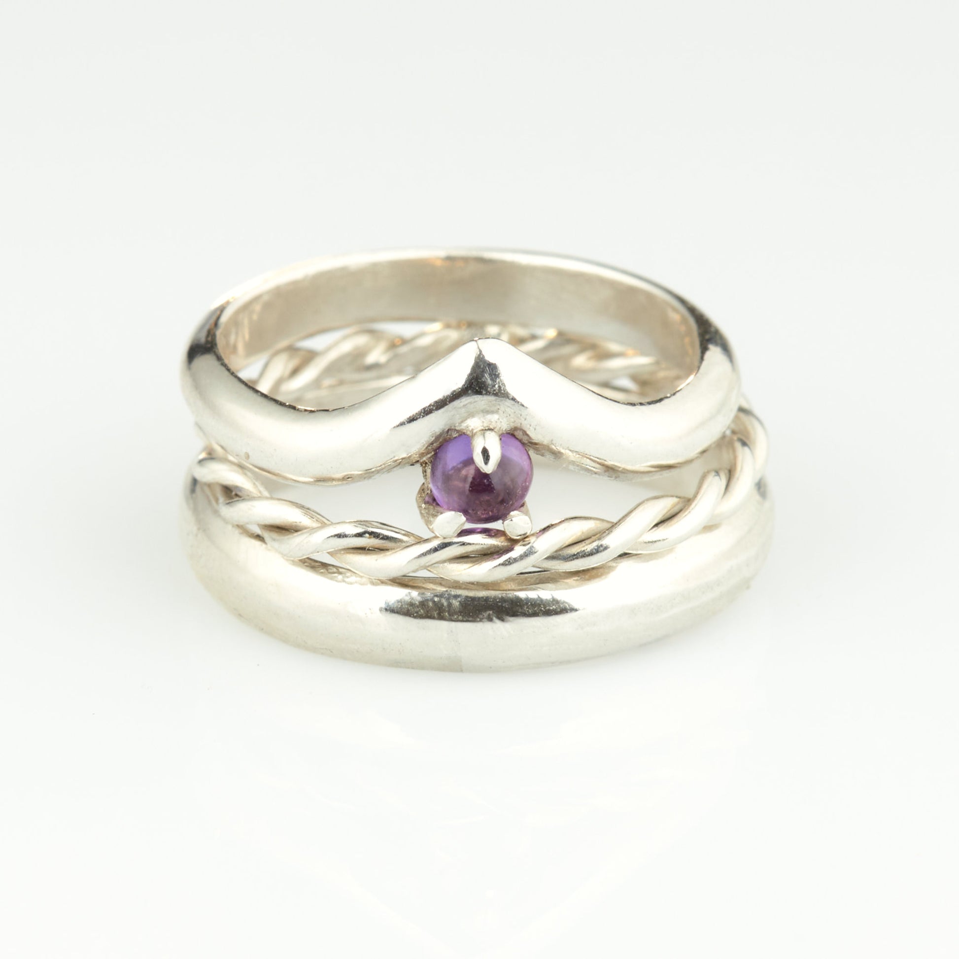 Handgefertigtes Ehering-Set aus 925 Silber auf Leder. 3-teiliges Damen-Set bestehend aus einem 3mm Wishbone-Ring mit Amethyst und einem 2mm Kordelring. Daneben ein massiver 4mm Herrenring im Halbrund-Profil. Zeitloses Design mit lila Edelstein für die Hochzeit. SEO-Keywords: Wishbone Eheringe Silber, Amethyst Trauringe Set, handgefertigte Silberringe, 925 Sterlingsilber Schmuck, Kordelring Hochzeit. Sichtbare Details der hochwertigen Handarbeit und Steinbesetzung.