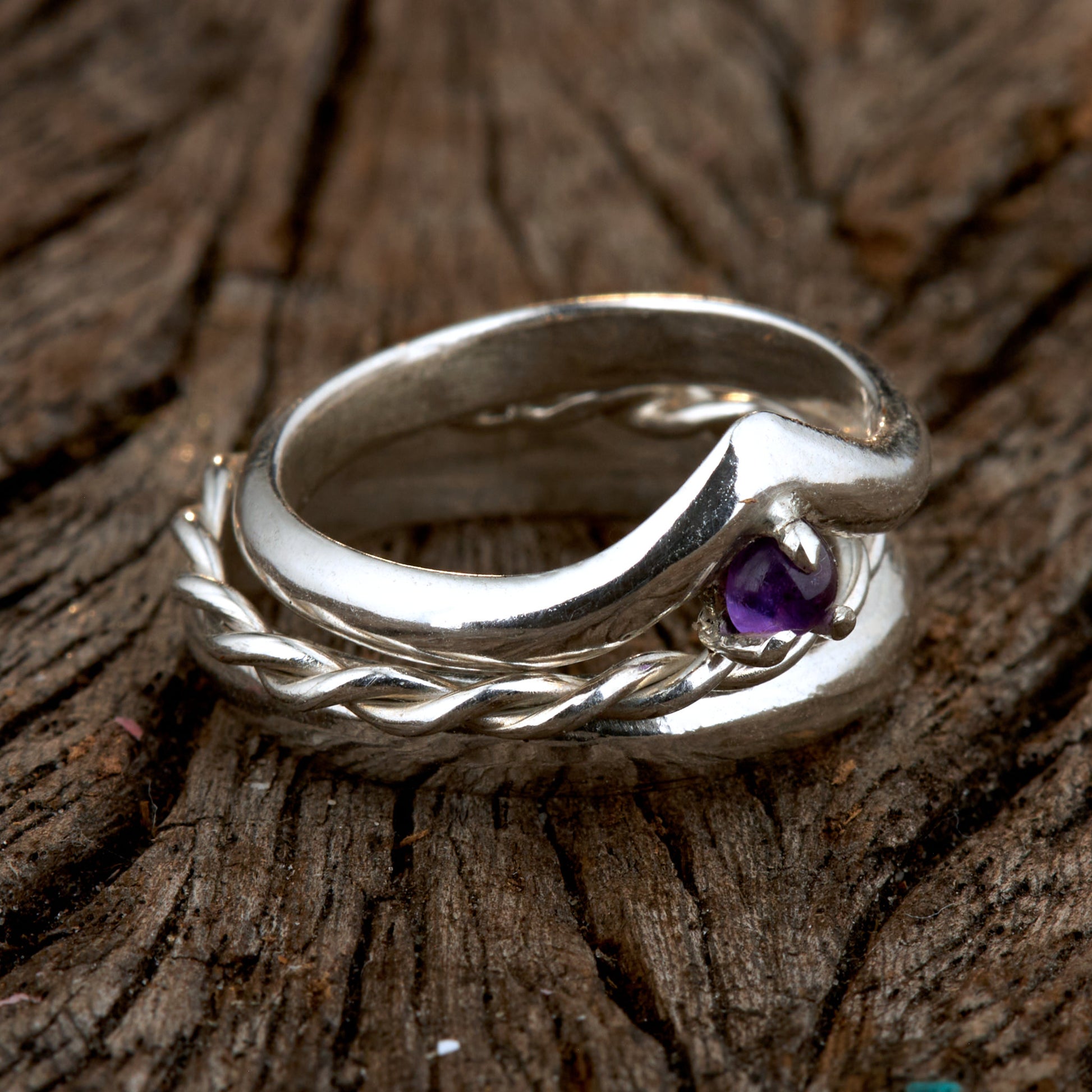 Handgefertigtes Ehering-Set aus 925 Silber auf Leder. 3-teiliges Damen-Set bestehend aus einem 3mm Wishbone-Ring mit Amethyst und einem 2mm Kordelring. Daneben ein massiver 4mm Herrenring im Halbrund-Profil. Zeitloses Design mit lila Edelstein für die Hochzeit. SEO-Keywords: Wishbone Eheringe Silber, Amethyst Trauringe Set, handgefertigte Silberringe, 925 Sterlingsilber Schmuck, Kordelring Hochzeit. Sichtbare Details der hochwertigen Handarbeit und Steinbesetzung.